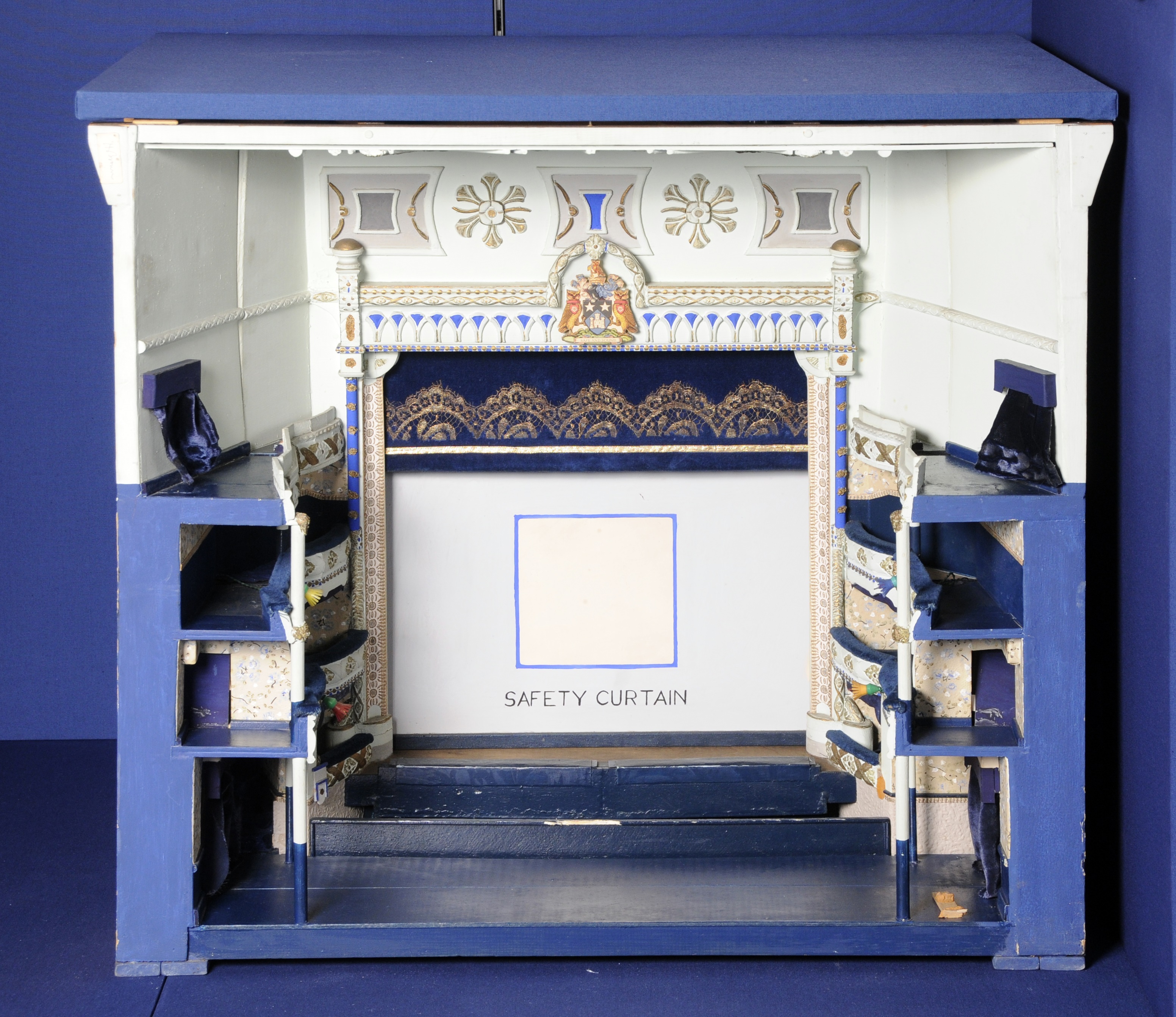 Model theatre painted in blue, white and gold.  It has a stage with a safety curtain and the stage curtain and stalls along the side for seats.