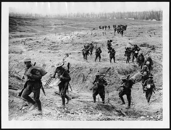A line of men walking across a bare slope, carrying all the gear needed to set up a new barbed-wire line.
