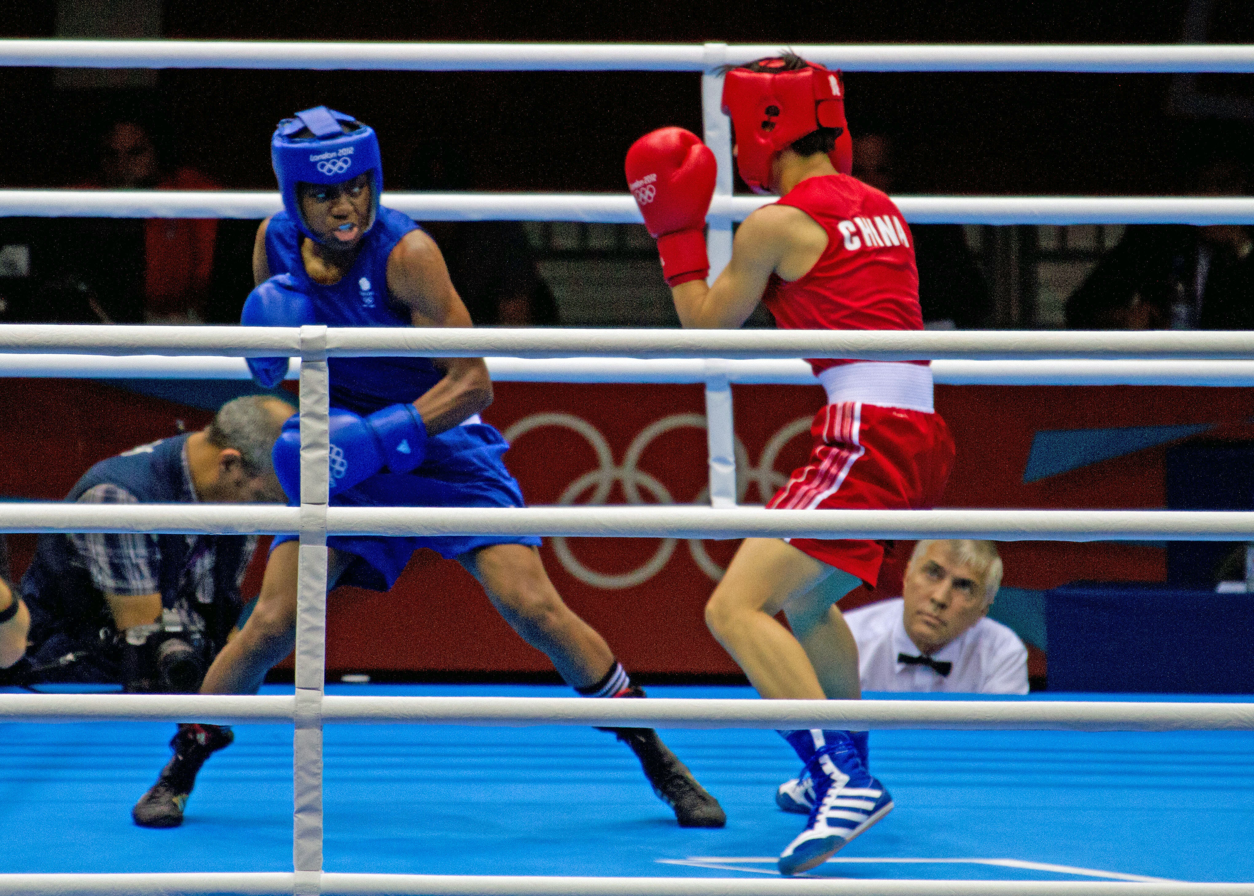 Two female boxers in a boxing ring, one in blue kit one in red kit
