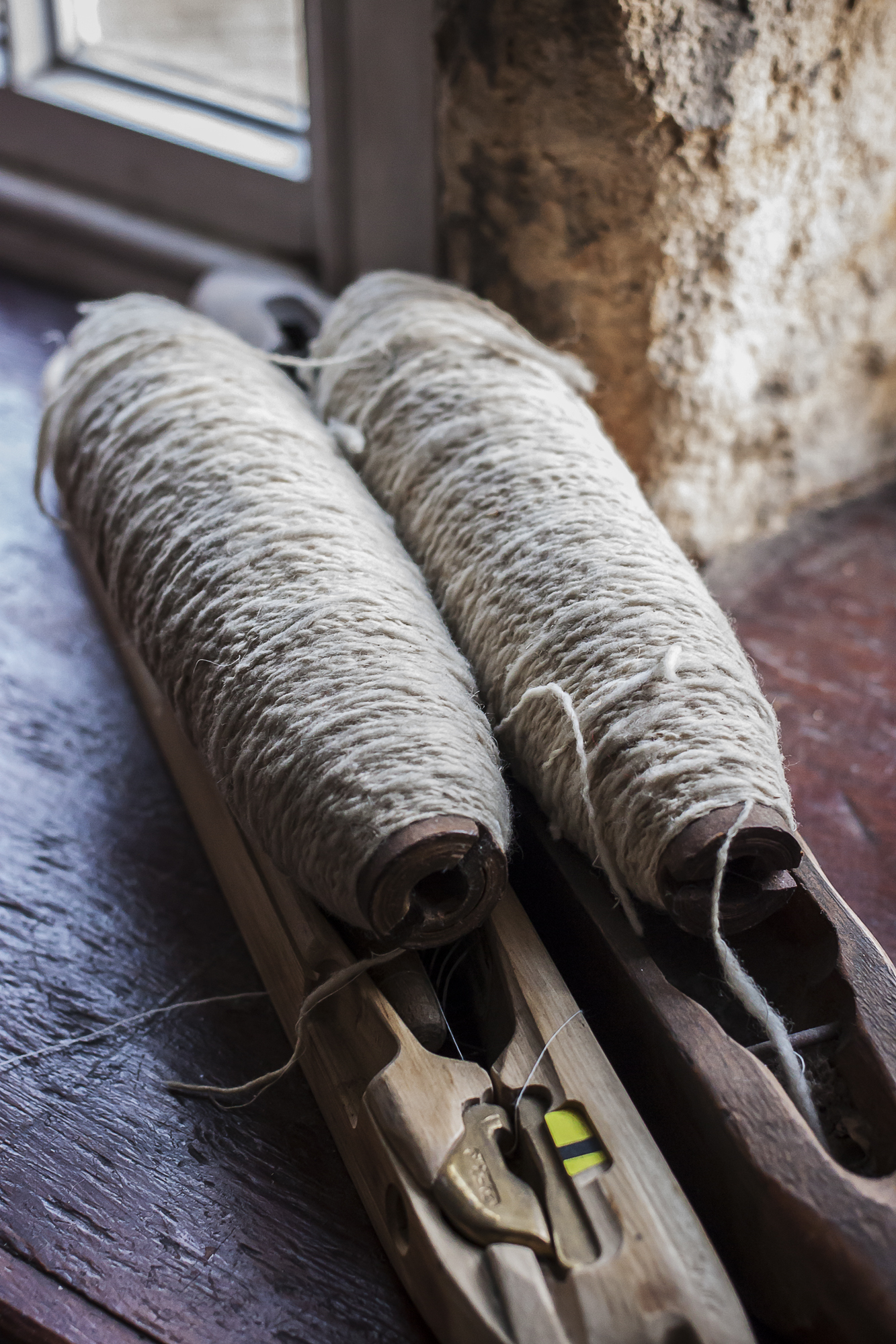 Two bobbins wound with natural coloured woollen yarn, sitting on top of wooden shuttles