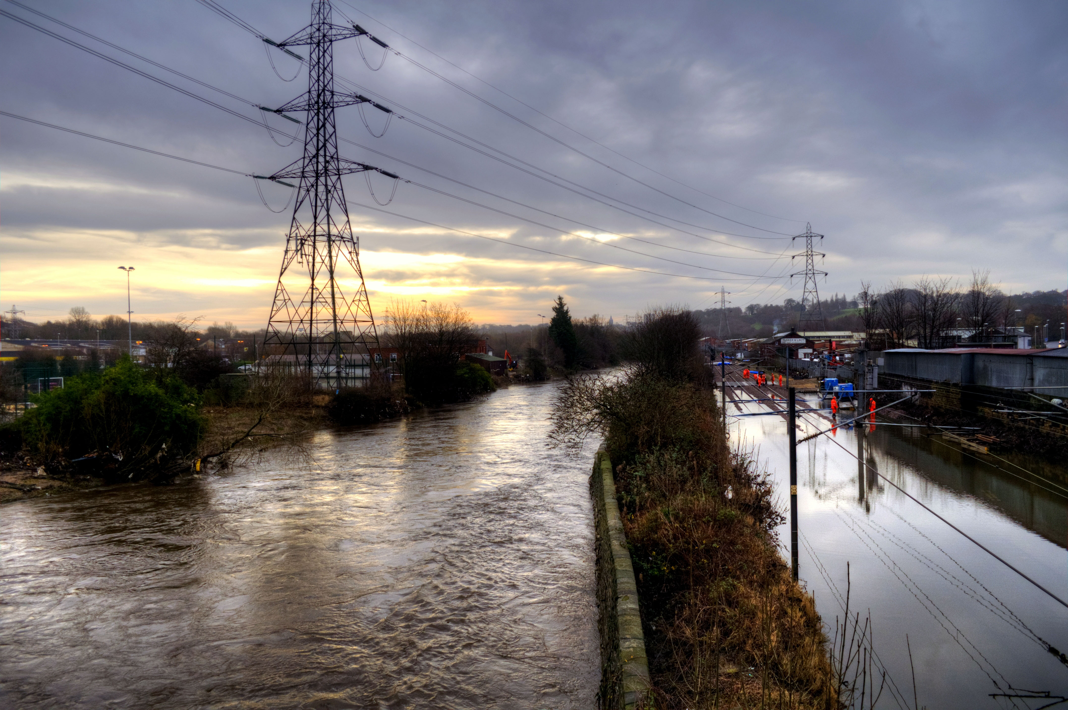 Colour photograph showing the railway line at Leeds submerged underwater.  The river runs by with just a narrow strip of vegetation in between.
