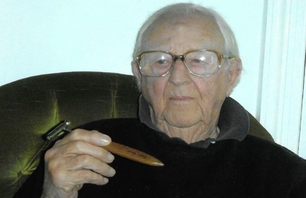 Colour photograph of an older man holding a razor with a home made wooden handle