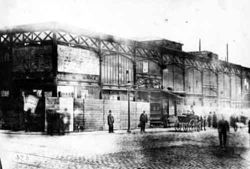 Black and white photograph showing one side of Kirkgate market.  Men and a horse and cart are in the street outside.