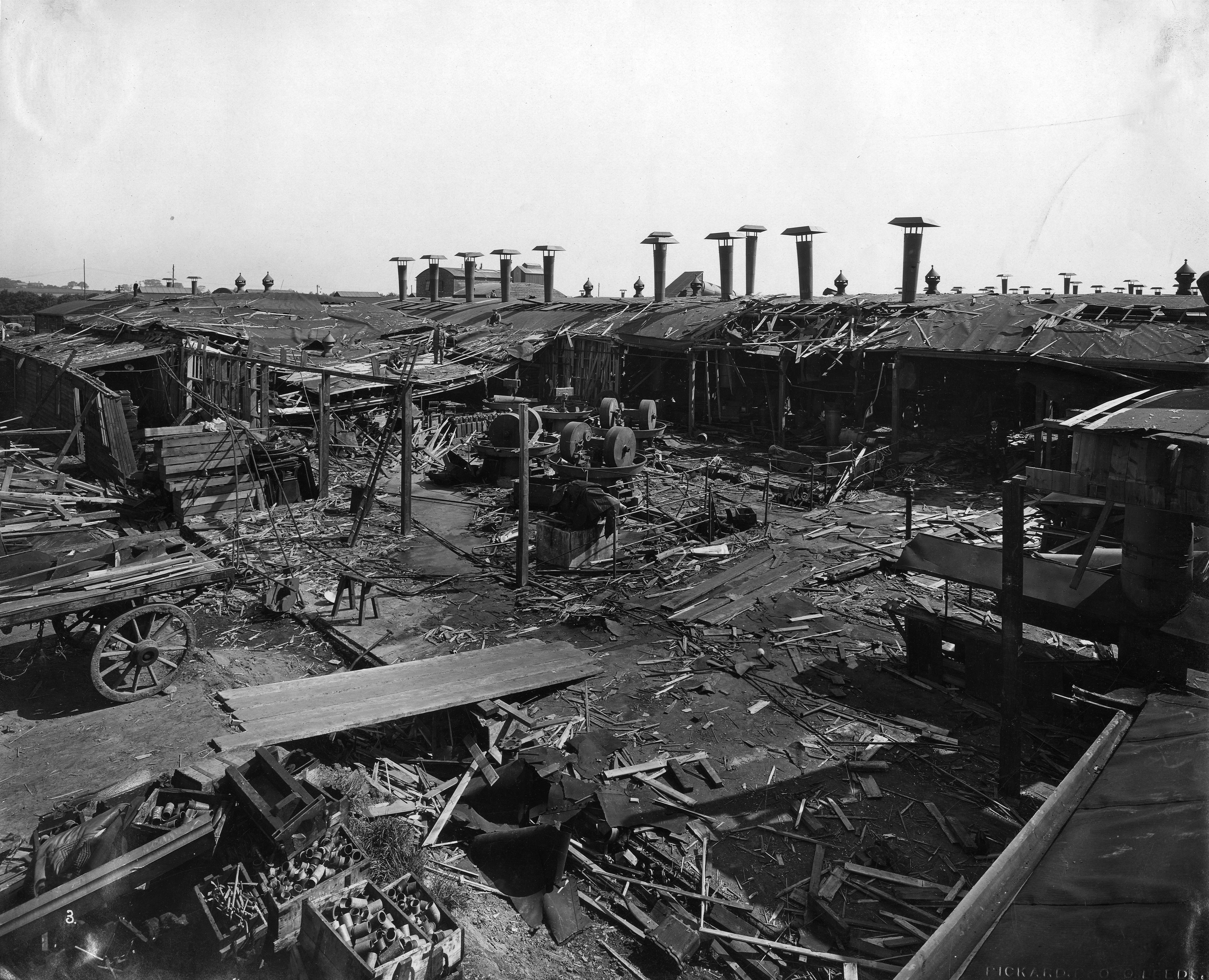 Black and white photograph showing extensive damage to wooden factory sheds