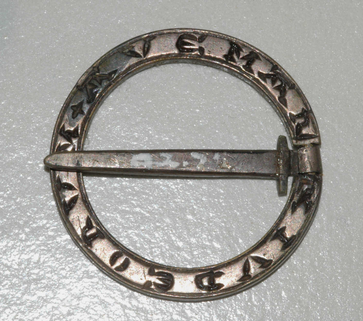 Antique metal belt buckle on white background, circular with engraved stars and text around the edge, featuring a central bar for fastening.