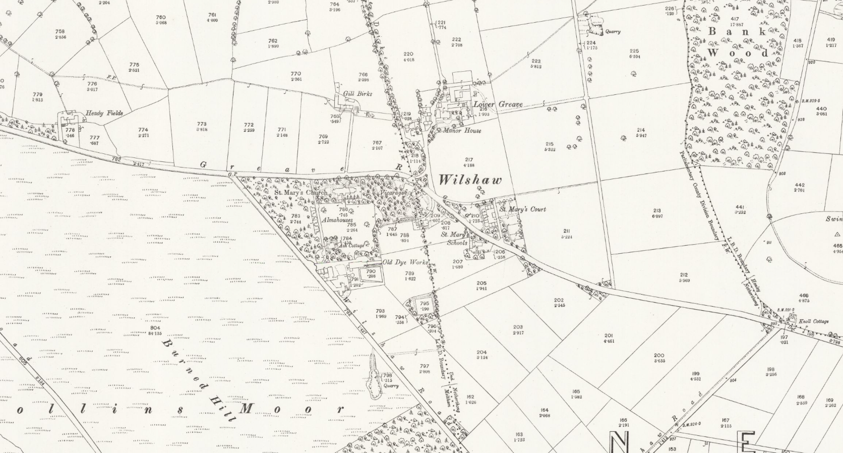 This black-and-white historical Ordnance Survey map shows the village of Wilshaw and its surroundings. Key landmarks include St. Mary’s Church in the southwest, with nearby Alms-houses and St. Mary’s Schools. The Old Dye Works is located just south of the village centre. Other notable buildings include the Vicarage, Manor House, and cottages such as Lower Greave and Gill Birks. The map also shows surrounding fields with names and acreages, wooded areas like Bank Wood, and features such as a quarry and Burnt Hill Moor to the west.