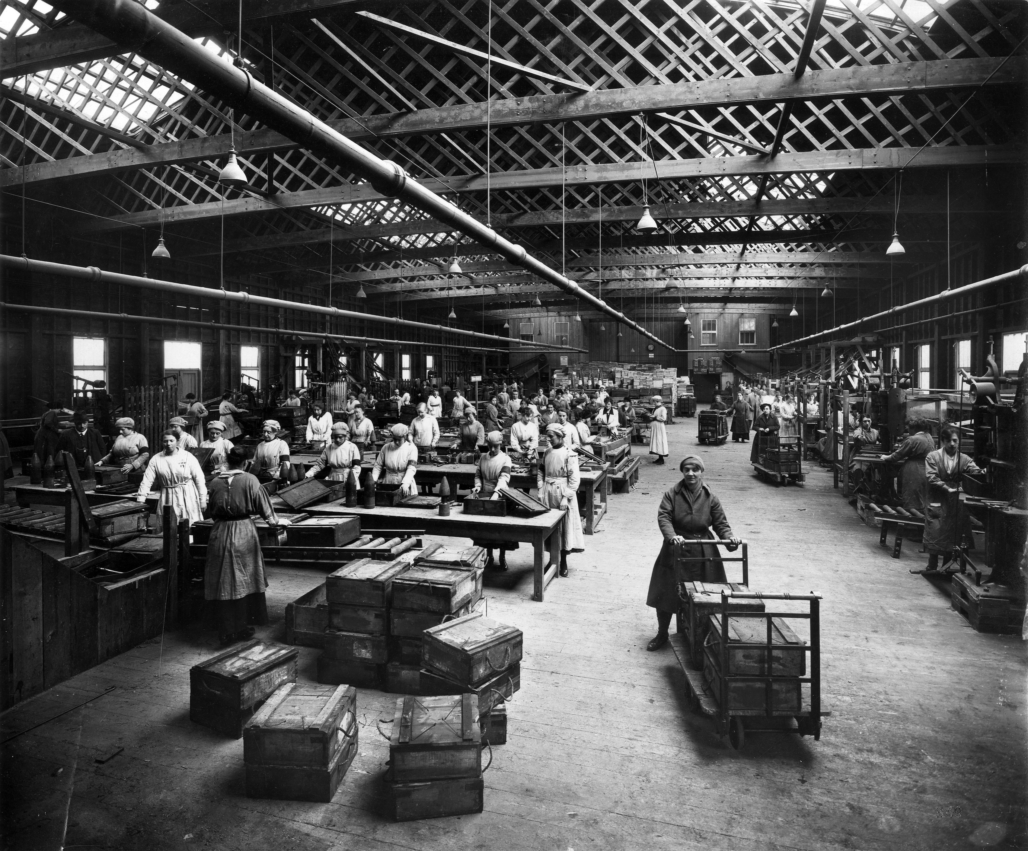 Black and white photograph showing interior of Barnbow No.1 Leeds National Filling Factory, several female workers visible with wooden crates and pallets containing bomb shells