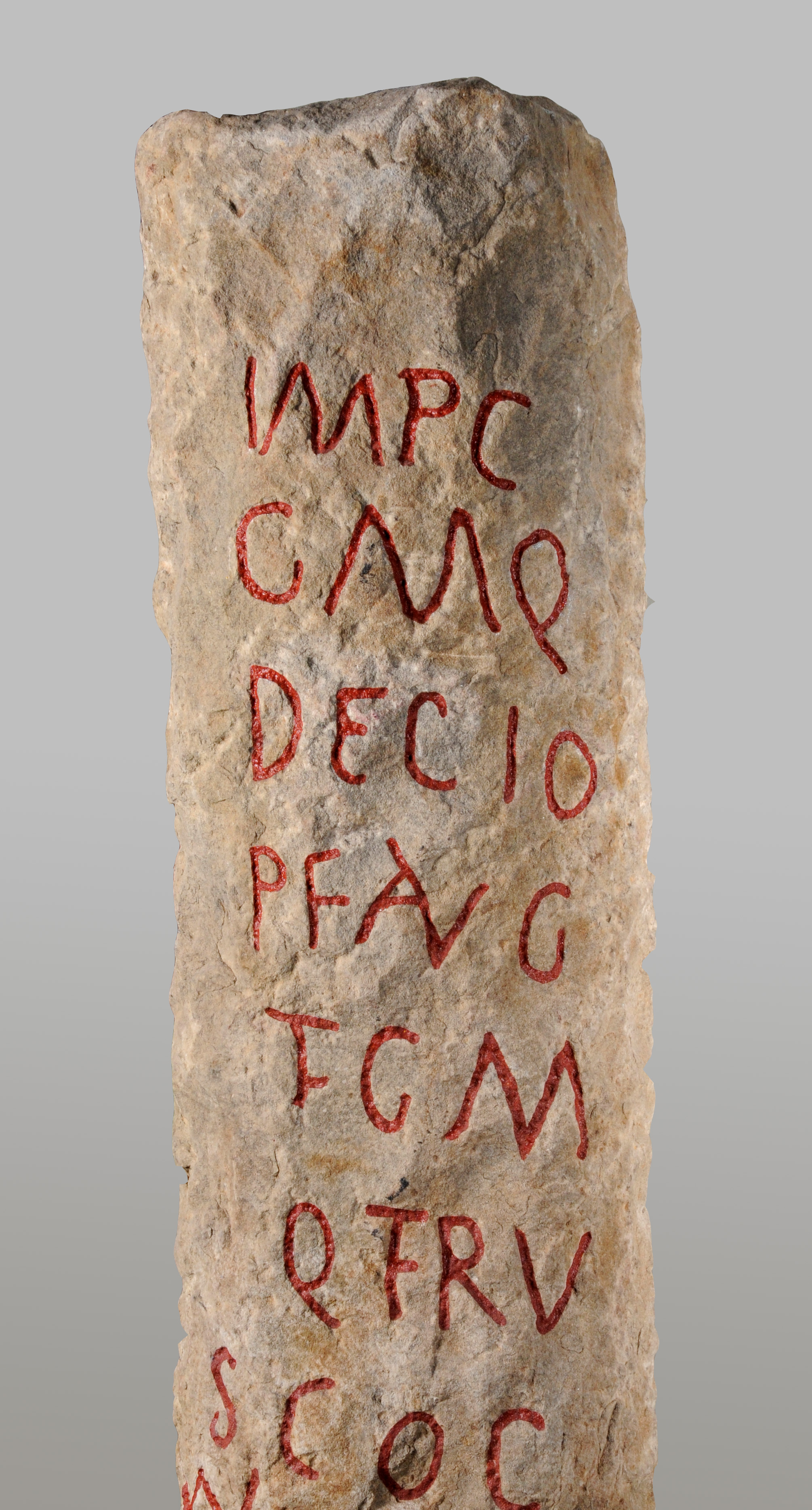 Colour photograph showing a worked block of stone carved with letters. The letters have ben infilled with red colour