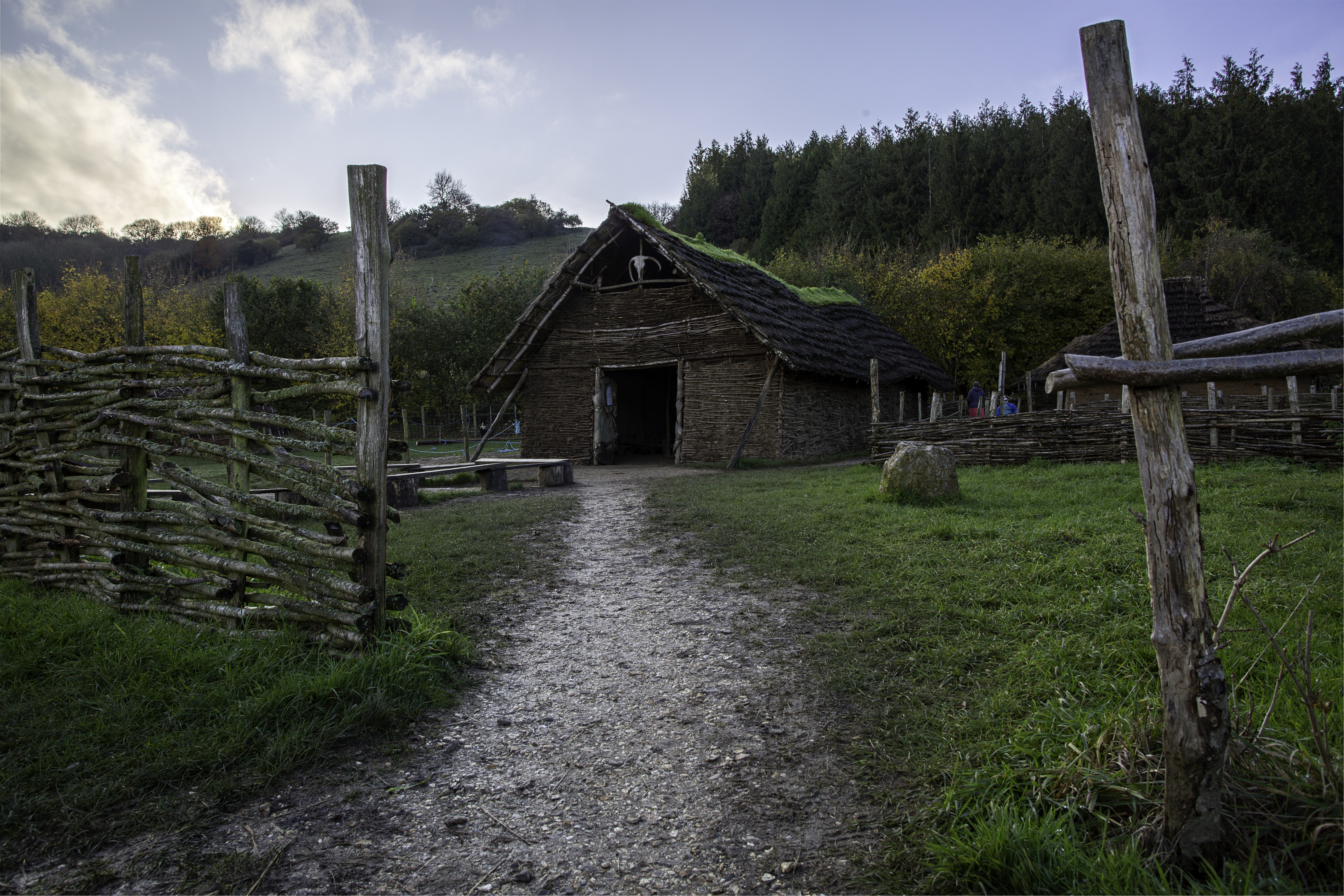 Stone Age Building Reconstruction Exterior view with path and wooden fencing, hill and trees in background