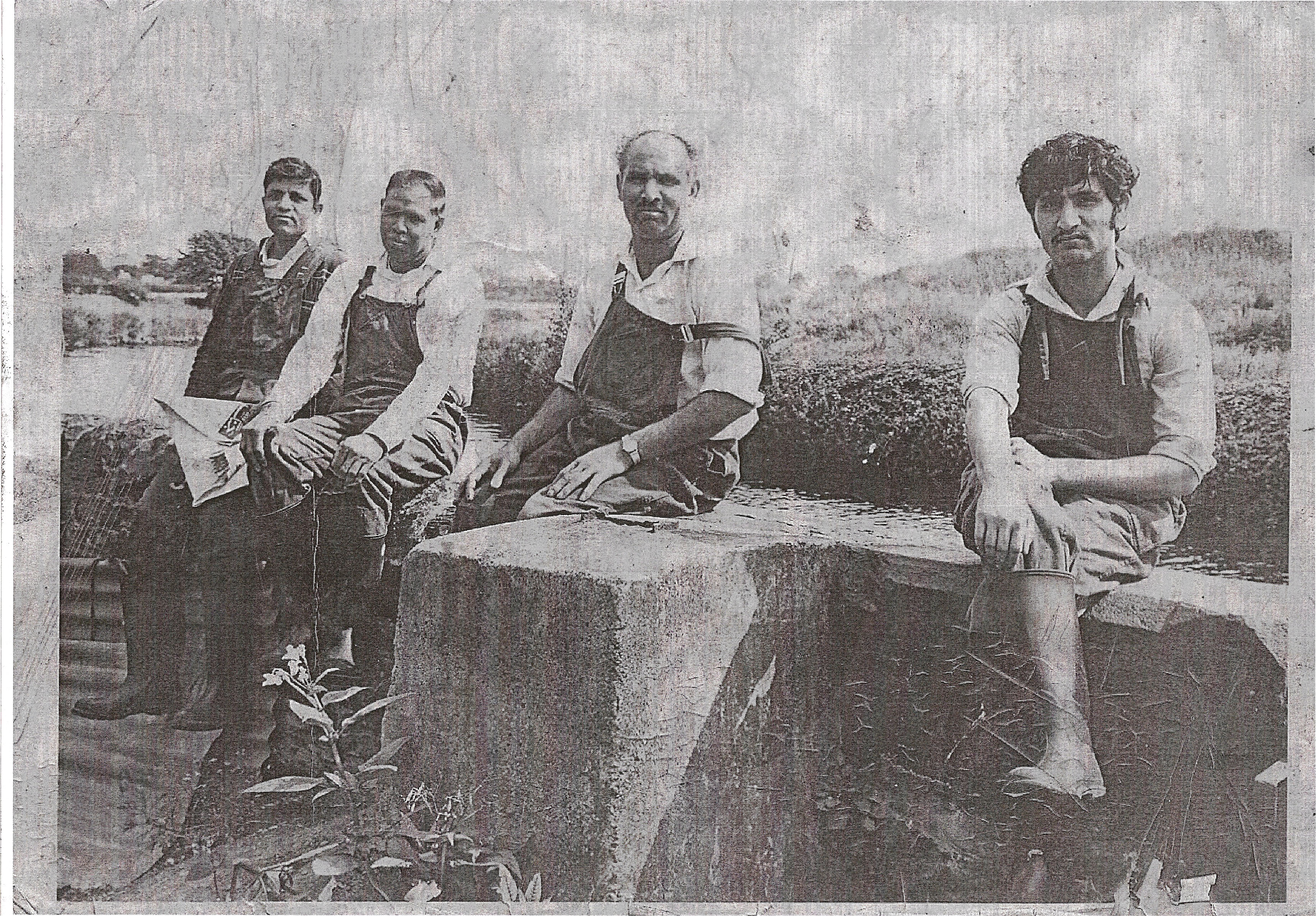 Black and white image of four men of Pakistani heritage wearing aprons and sitting outside
