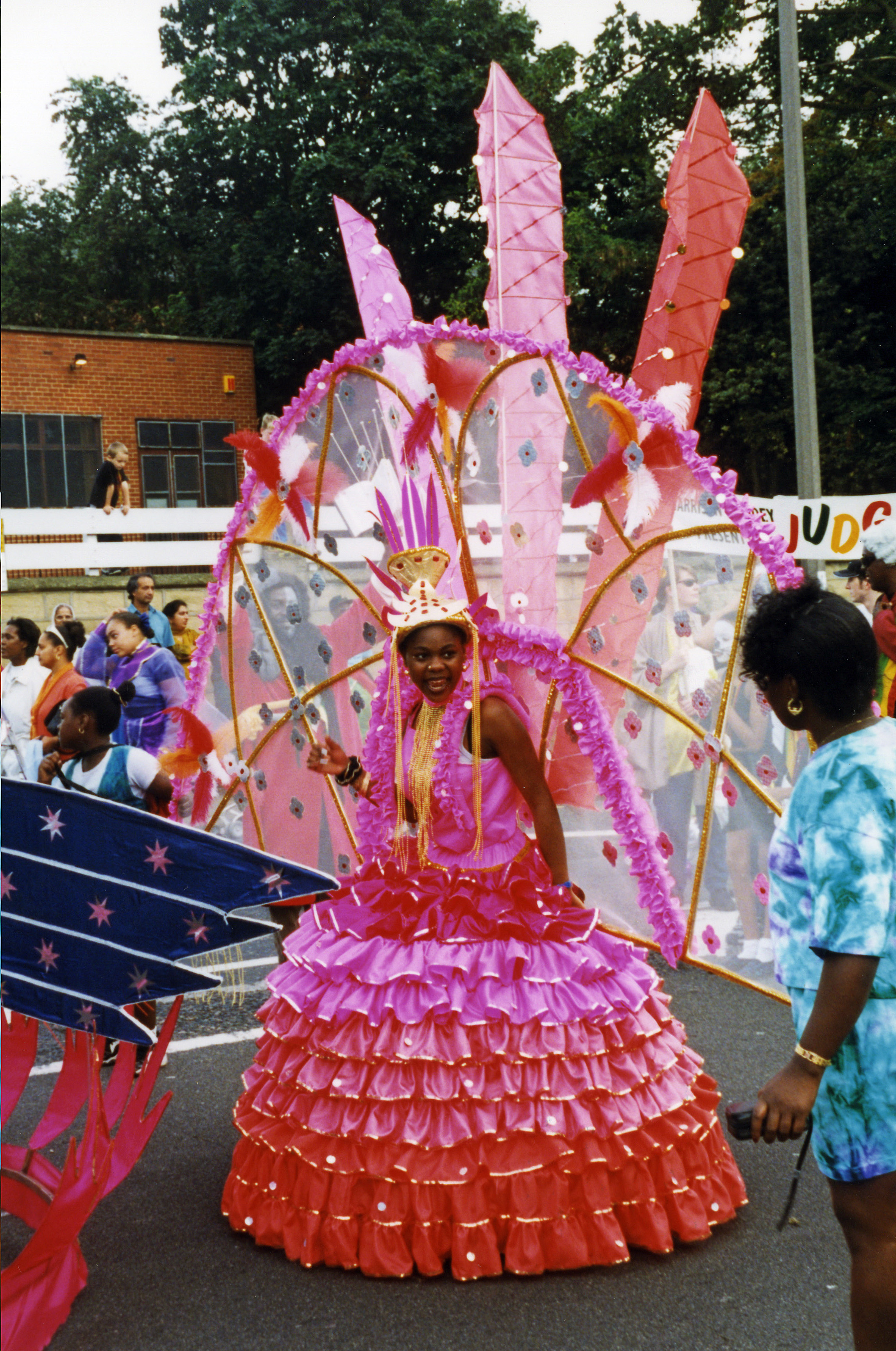 Colour photograph showing a young woman dressed in a pink carnival costume