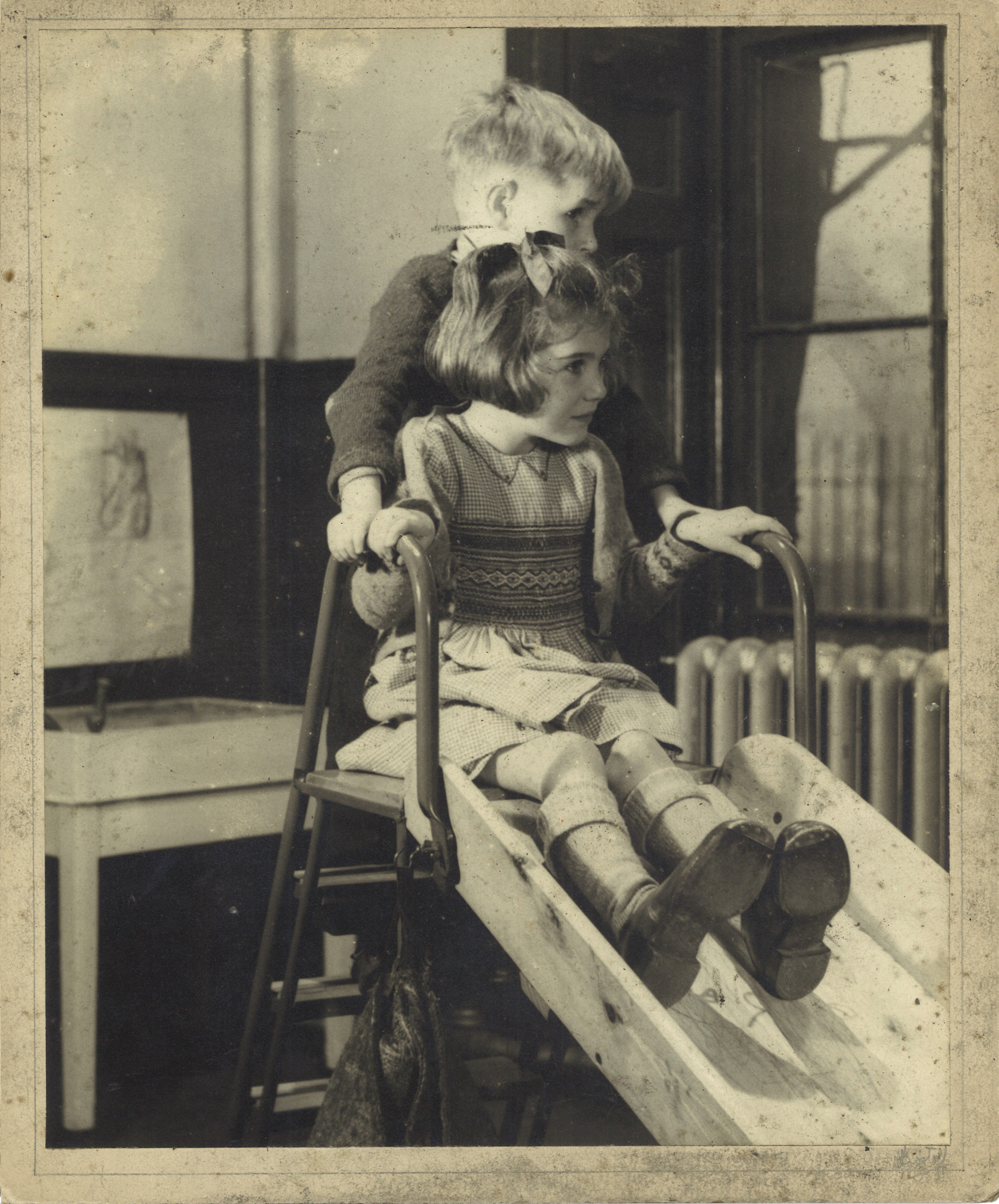 Black and white photograph showing a girl and a boy on a slide inside.