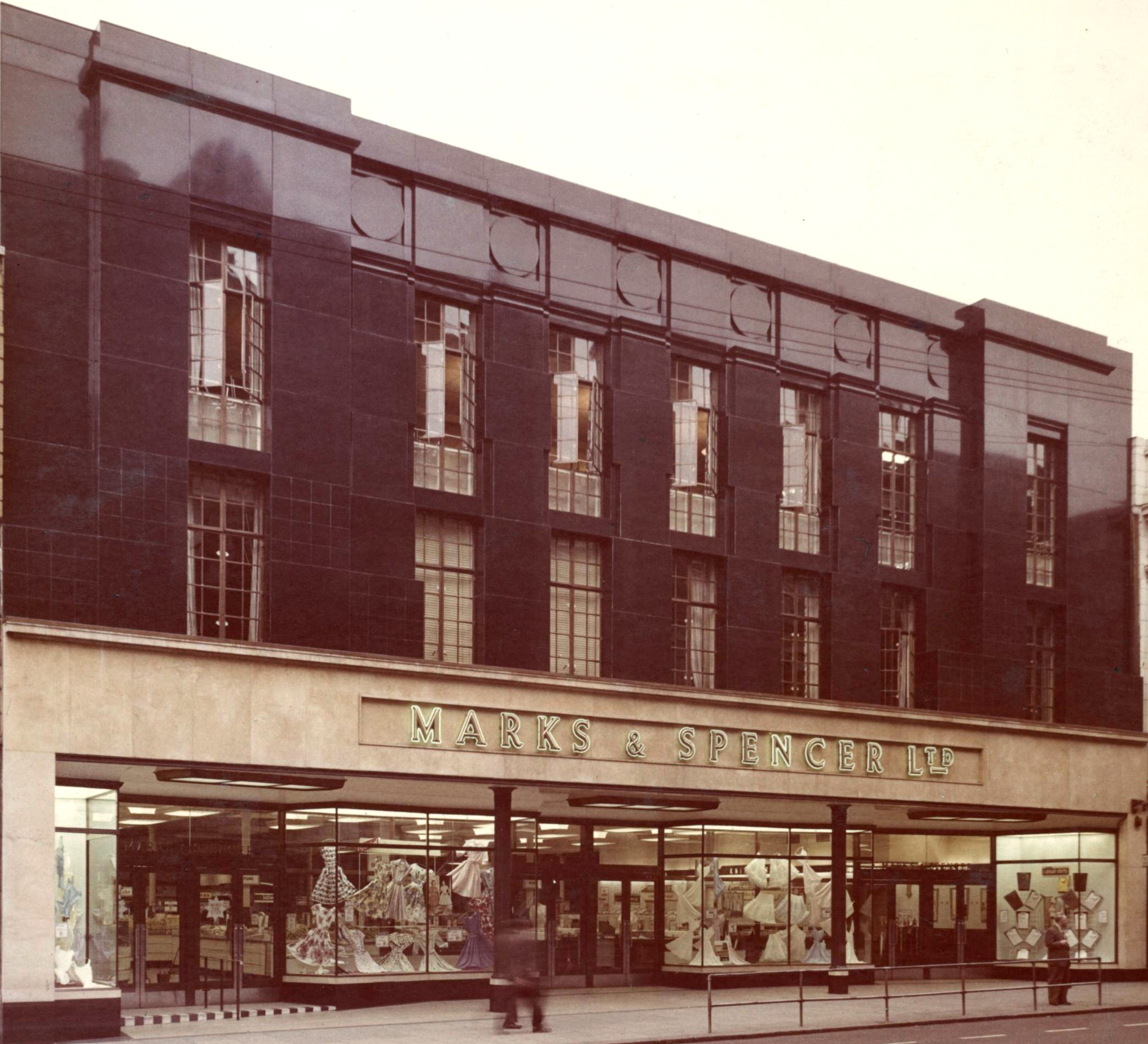 Exterior view of a Marks & Spencer store with a dark Art Deco-style façade and large display windows.