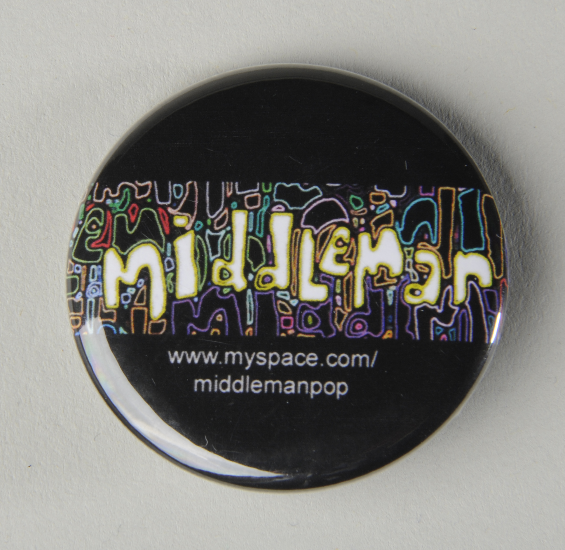 black buttonbadge with coloured wiggly lines across the middle and the word 'Middleman' written in white