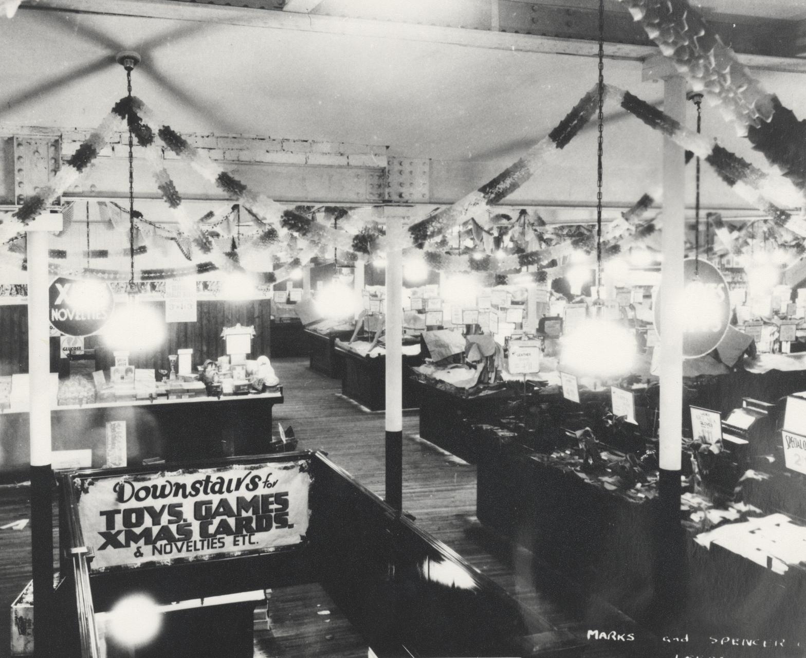 Black-and-white photograph of a decorated department store interior advertising toys and Christmas goods downstairs.