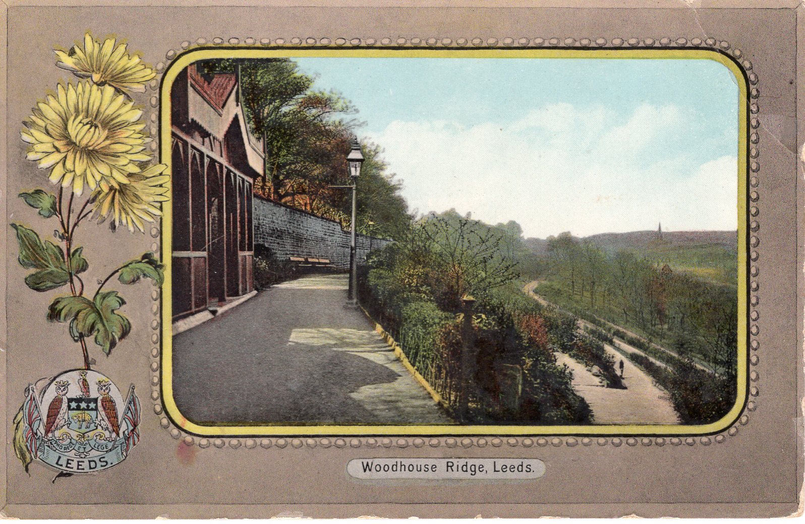 Colour image of a park. One path stretches ahead, with a brown wooden shelter and lamppost on the left. Another path slopes down to the tight and zig zags down the hill. Between the paths are plants and shrubs