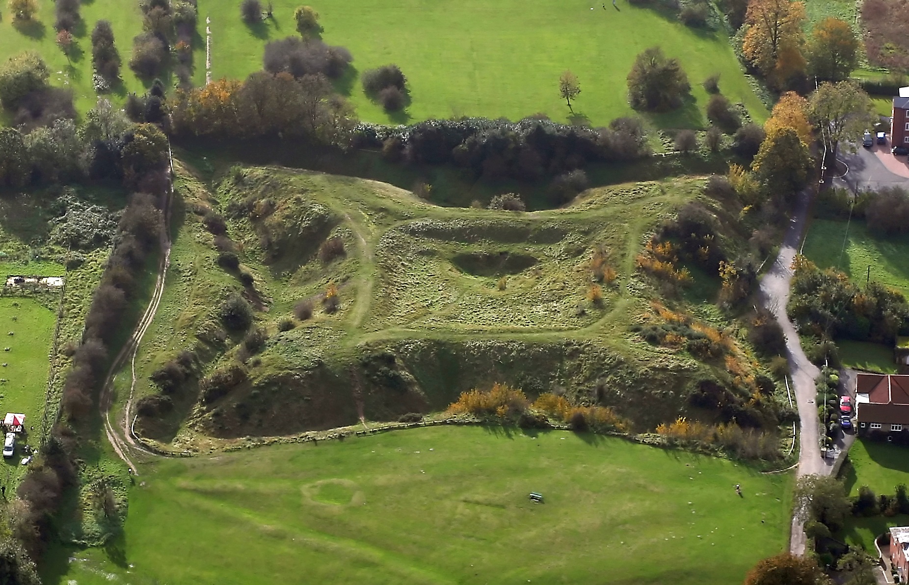 Aerial photo of raised earthworks on green hillside surrounded by ditches on its 4 sides