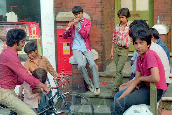 Colour photograph showing a group of boys  sitting outside a shop.