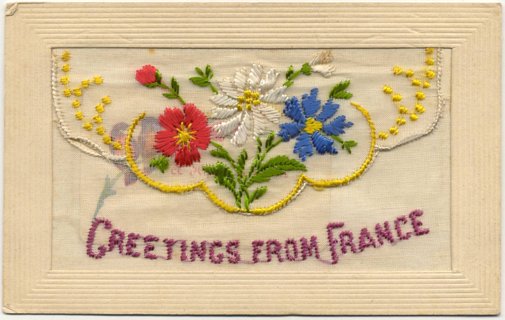 Vintage postcard with embroidered flowers in red, white and blue on a neutral fabric background, framed by a decorative cardboard edge. Embroidered text under the flowers reads "Greetings from France".