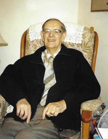 Colour photograph of an older man sitting in a chair smiling