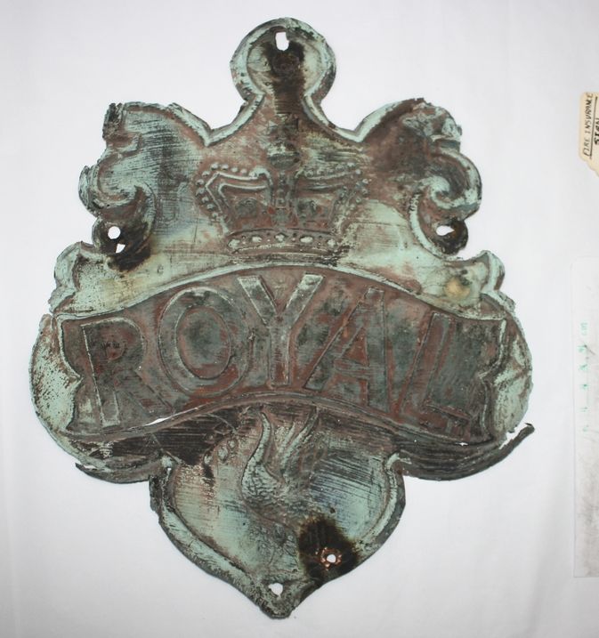 A weathered, ornate metal plaque with a crown emblem atop and the word "ROYAL" embossed below.