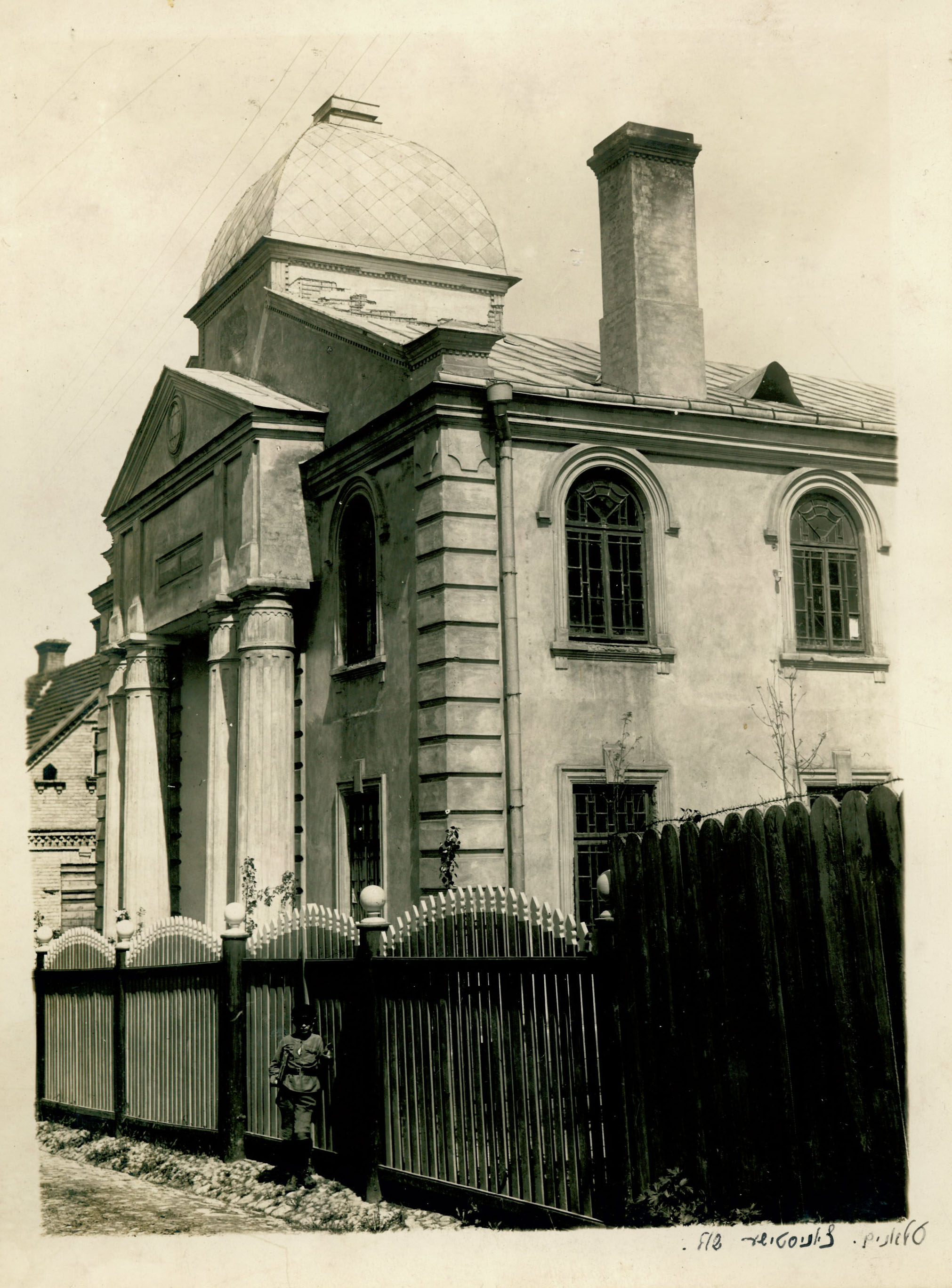 Black and white photo of exterior of a synagogue building with external fence and railings