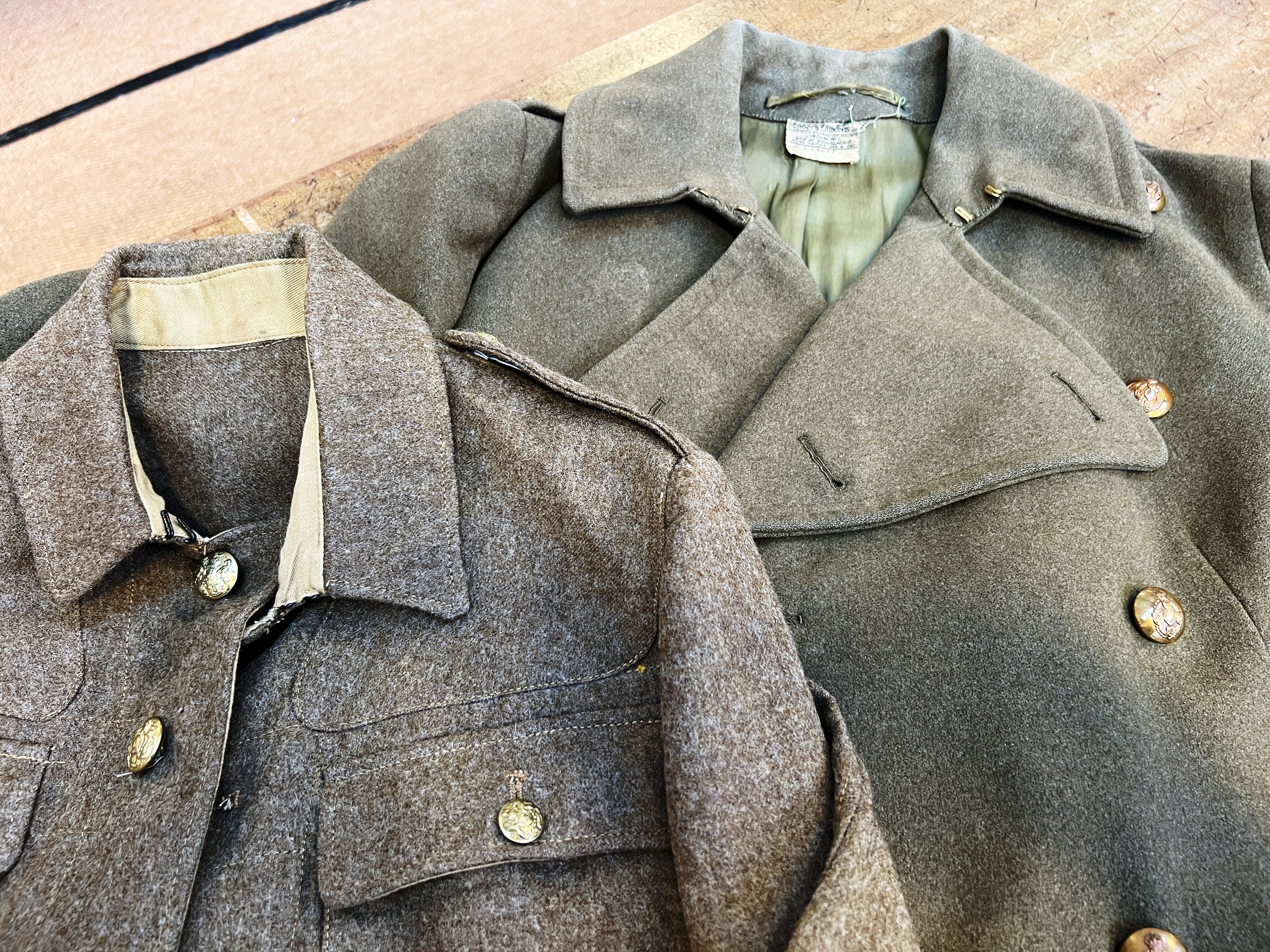 Two khaki army uniform jackets overlapping on a table