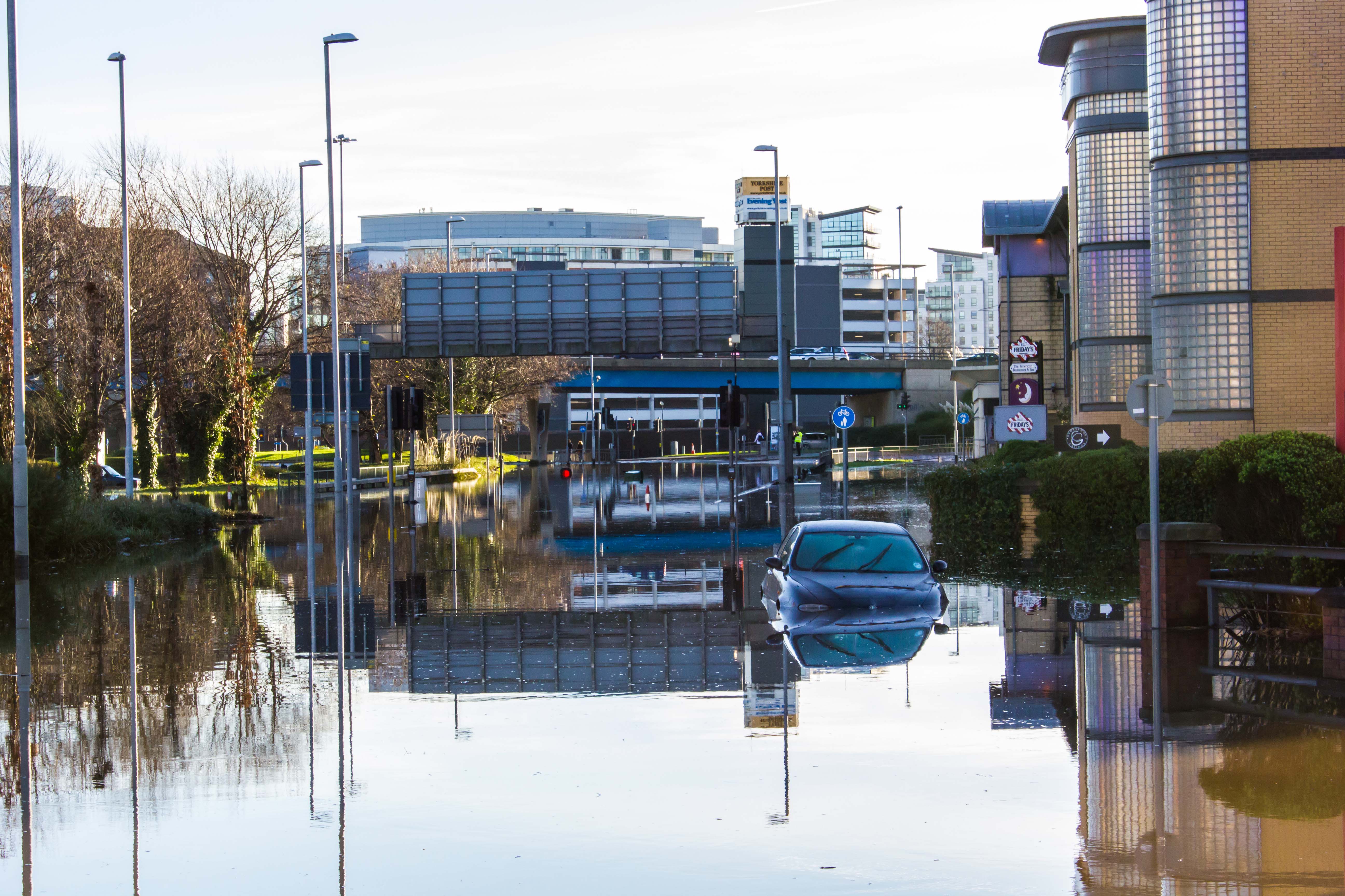 Photograph showing a wide road underwater, with a car half submerged in the street.