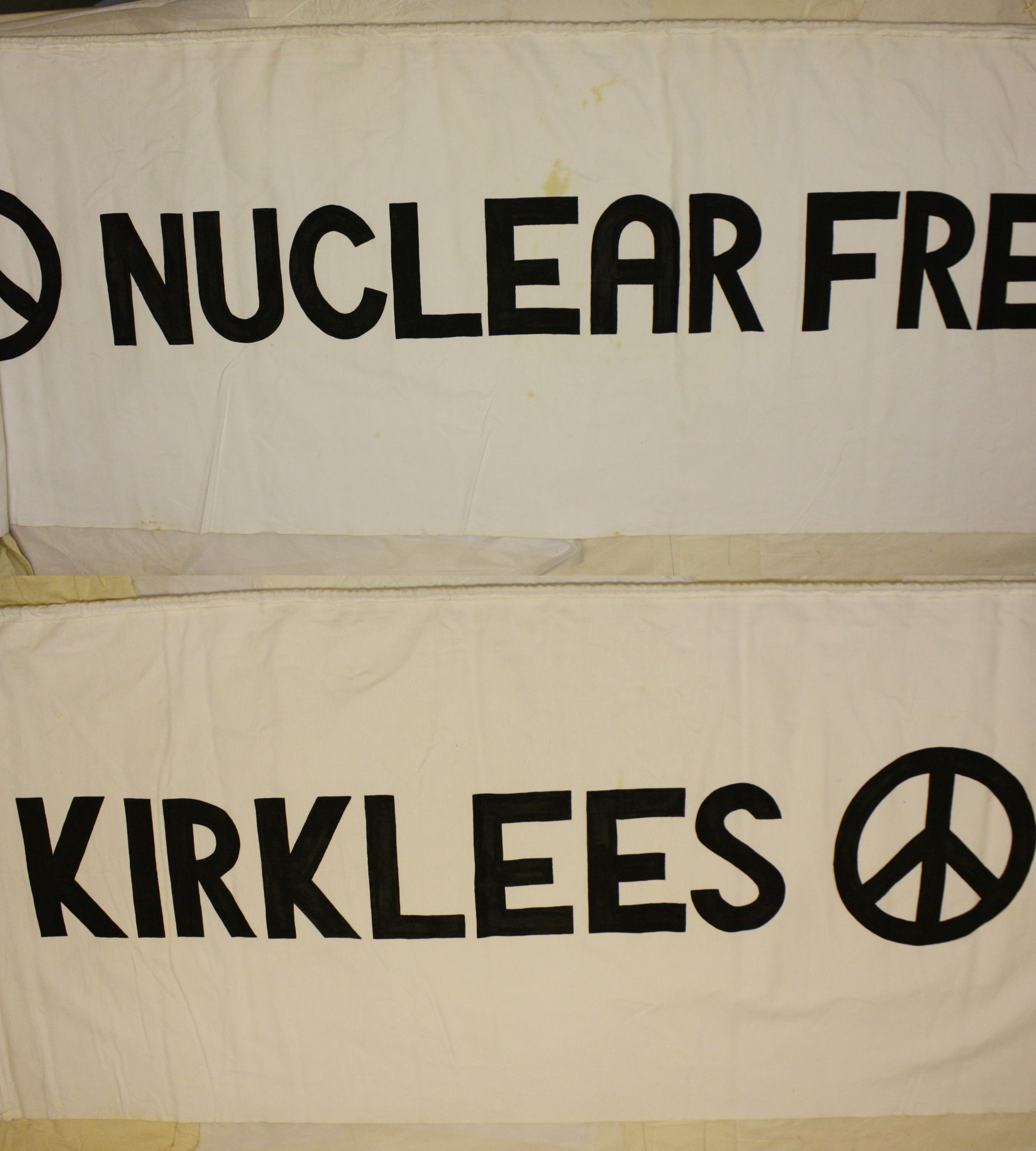 A white fabric banners with black text feature peace symbols. The top banner reads "Nuclear Free," and the bottom reads "Kirklees".