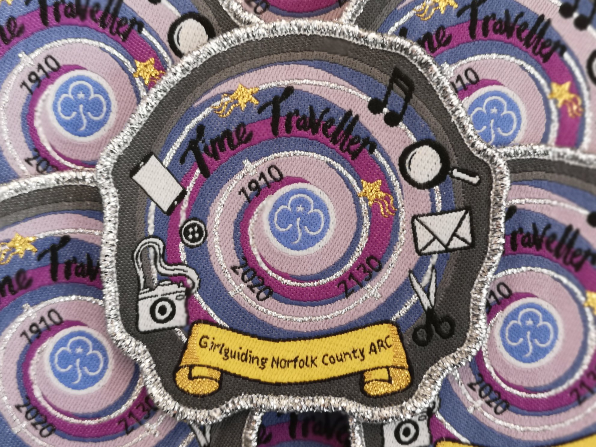 Colour photograph showing a grey, purple and blue swirl design with music notes, a camera, scissors and an envelope around the outside.