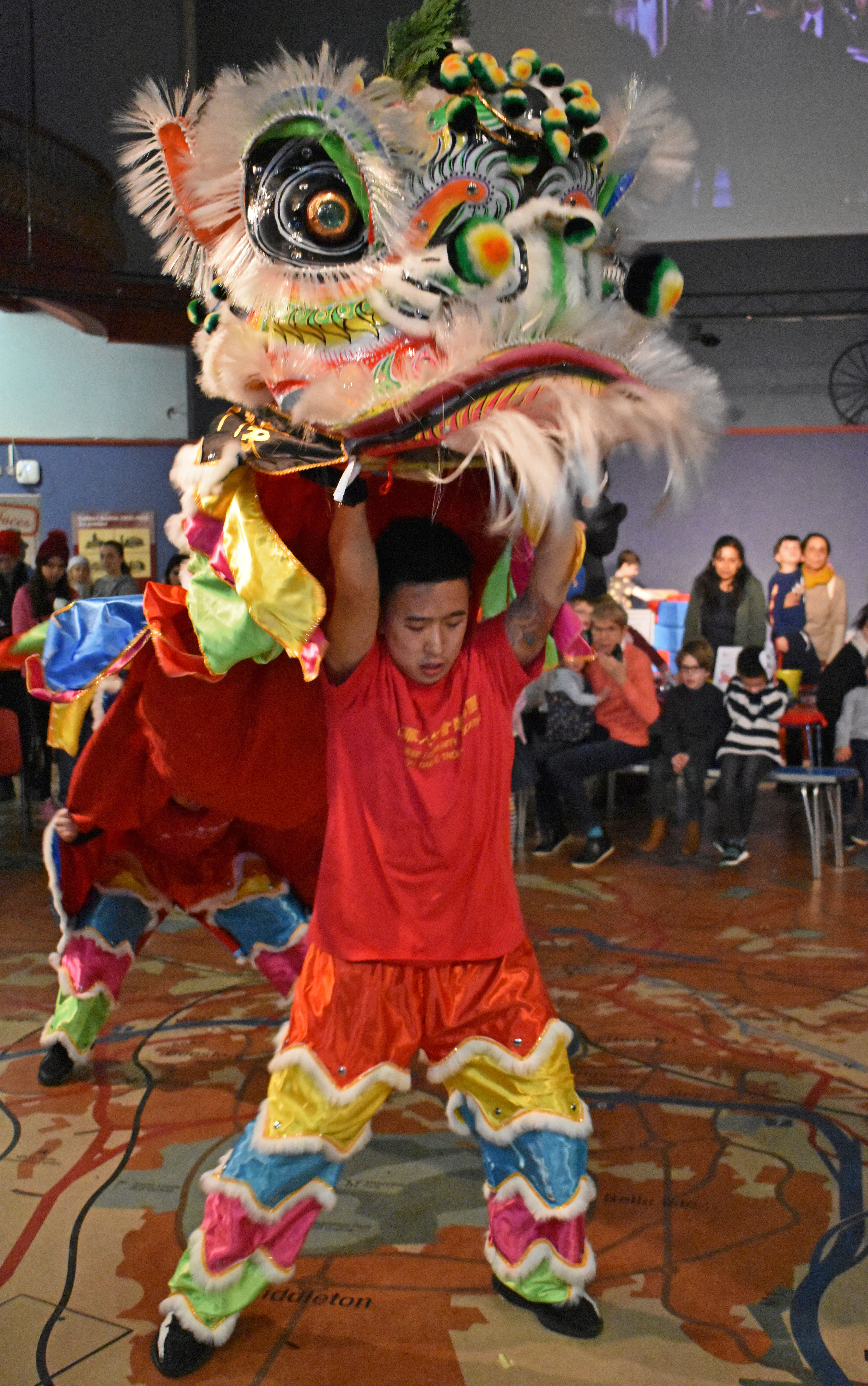 Photograph showing two men in costumes forming the legs of a large carnival style Chinese dragon puppet.