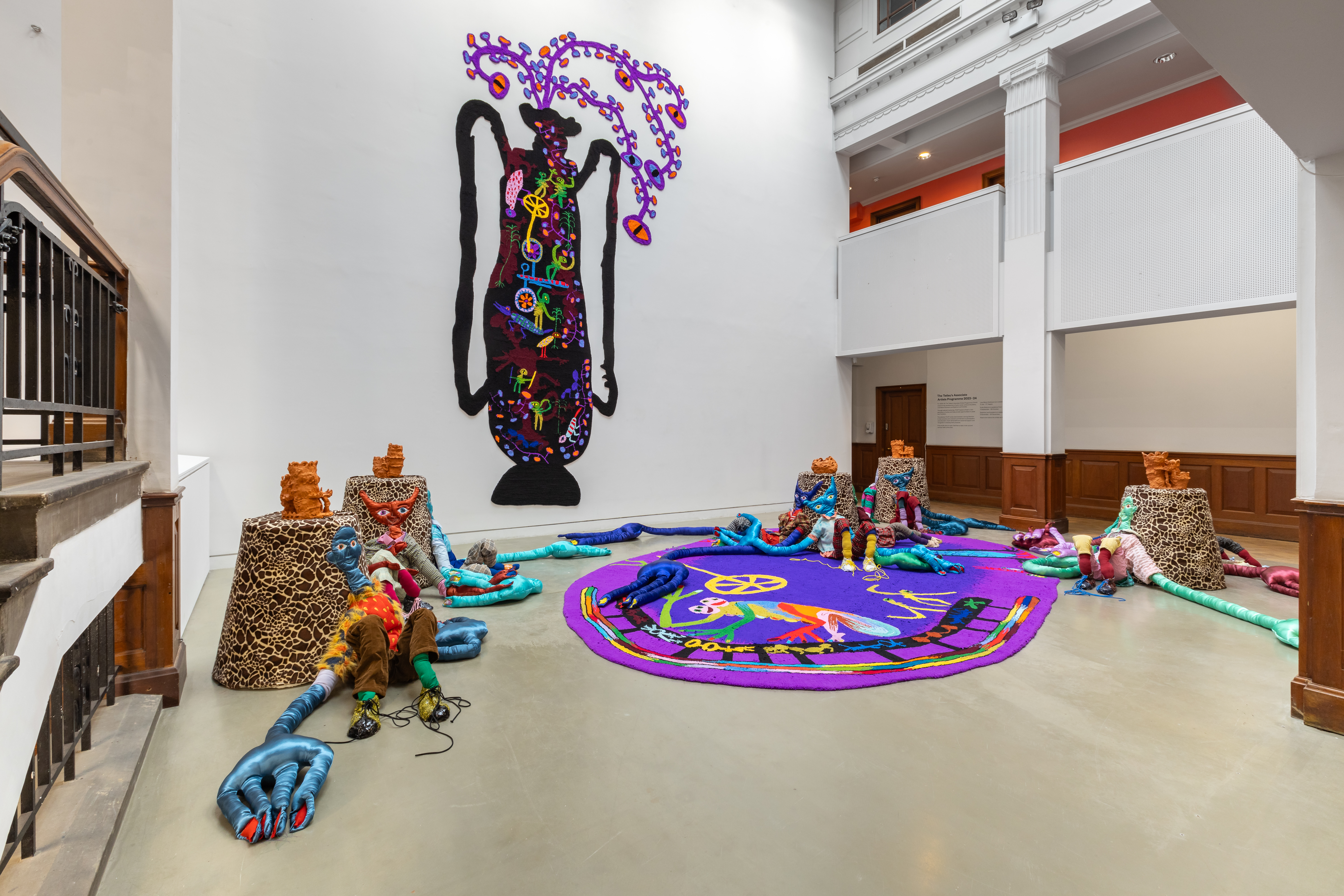 Artwork showing several alien figures made from colourful textiles in the atrium of a gallery