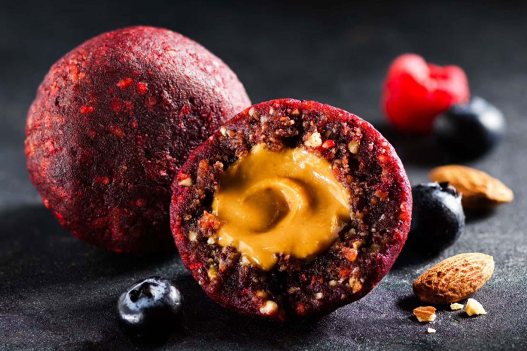 Colour photograph showing a red ball made from nuts and seeds, cut in half with a gooey centre