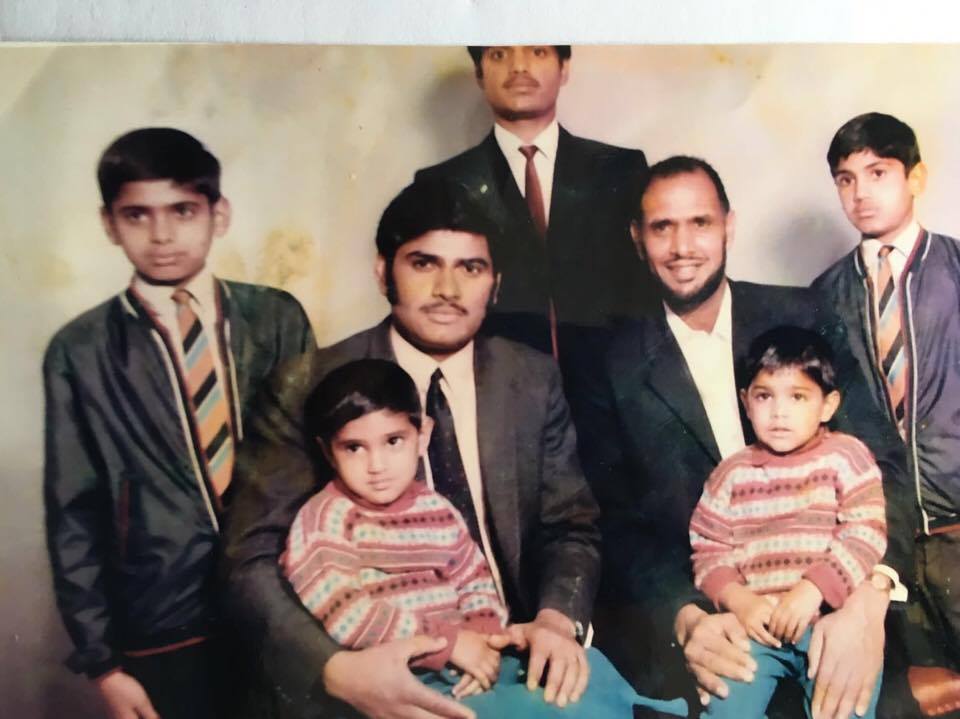 Colour photograph showing seven members of a family.  The men and older boys are in suits, the younger ones in matching outfits.
