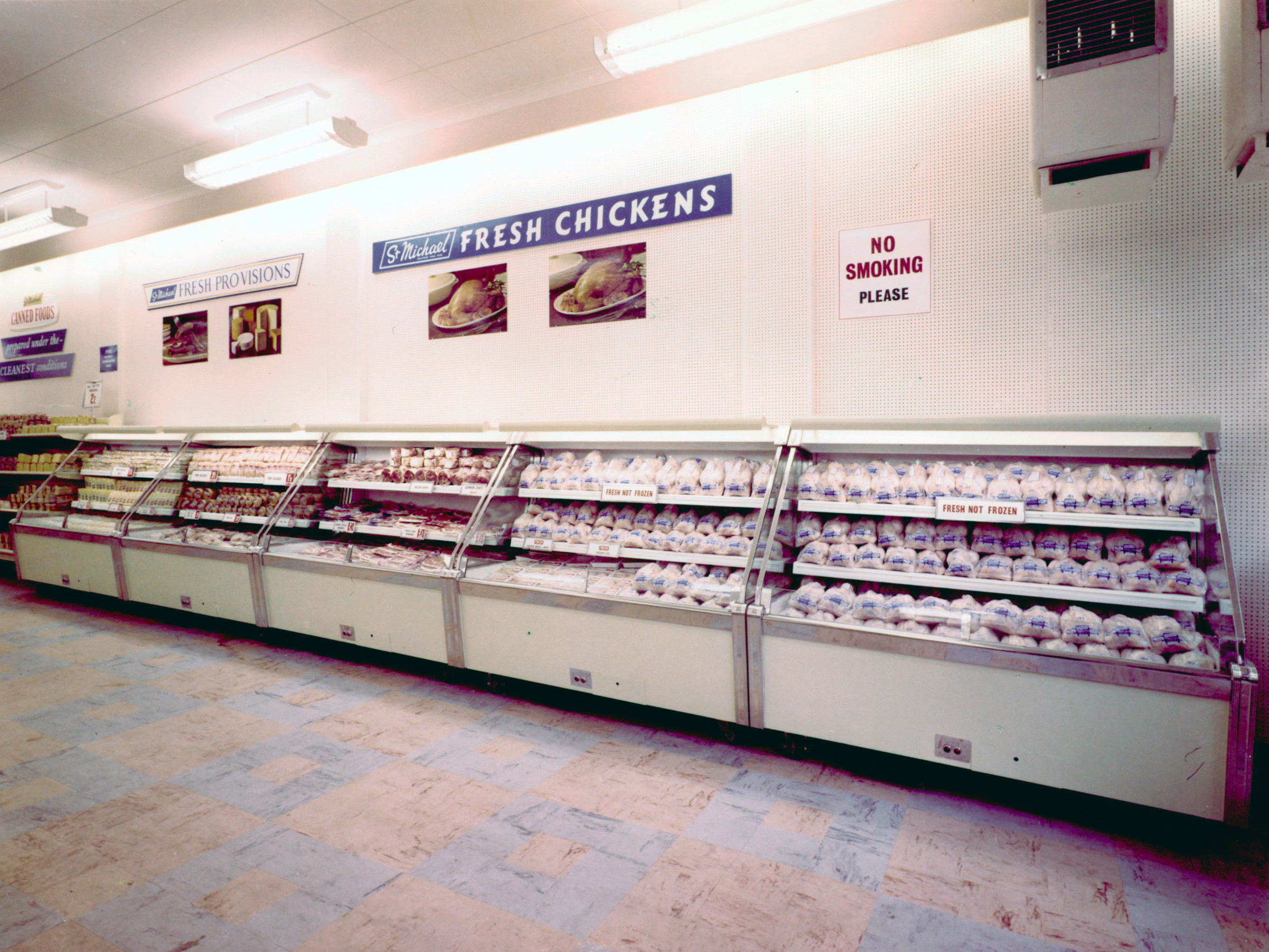 Refrigerated display cases filled with packaged fresh chickens in a supermarket, with signage reading “Fresh Chickens” and a “No Smoking Please” notice on the wall above.