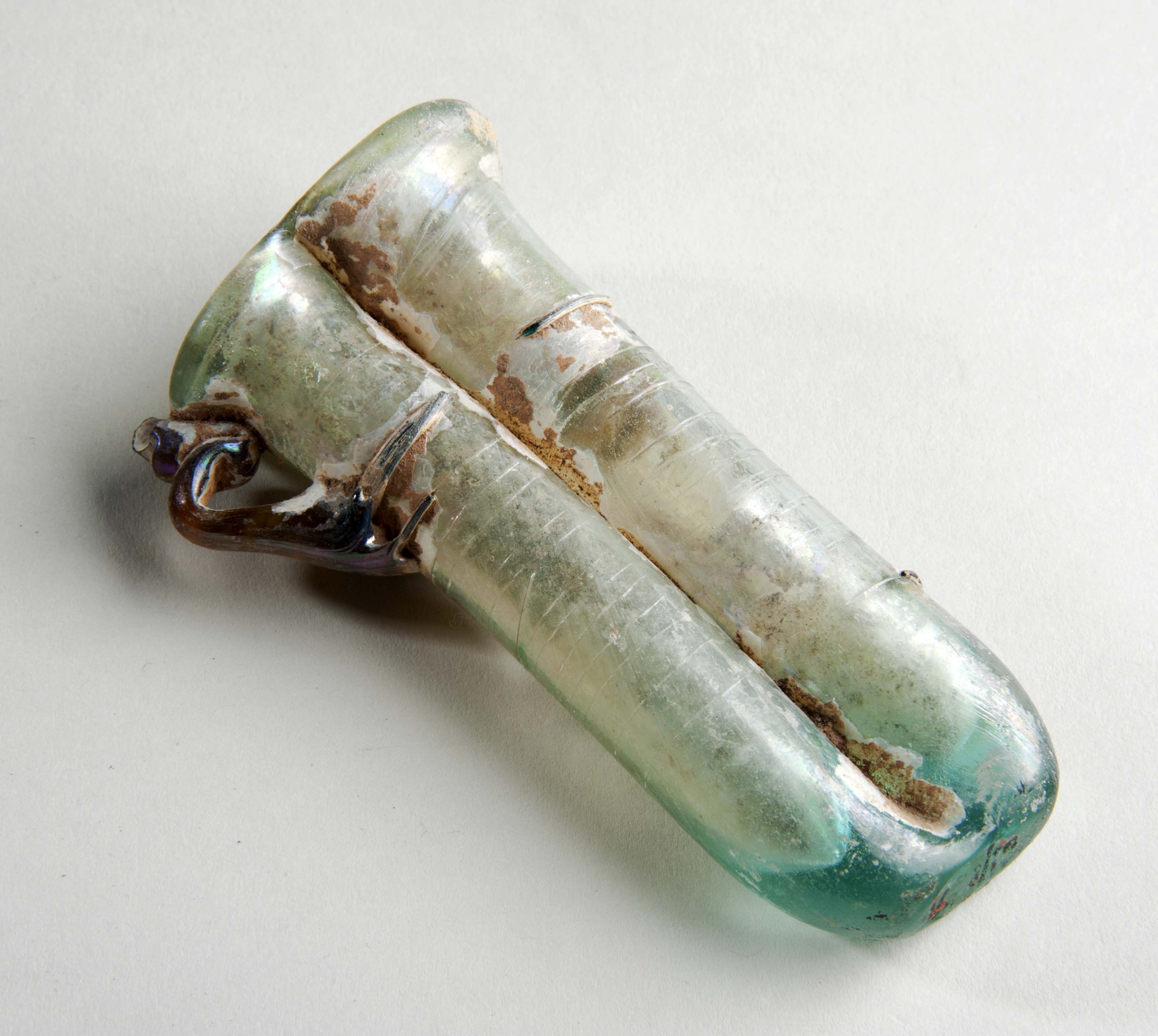 A Roman glass bottle. It has some rust, a blue base, and brown handle, and is otherwise white or grey.