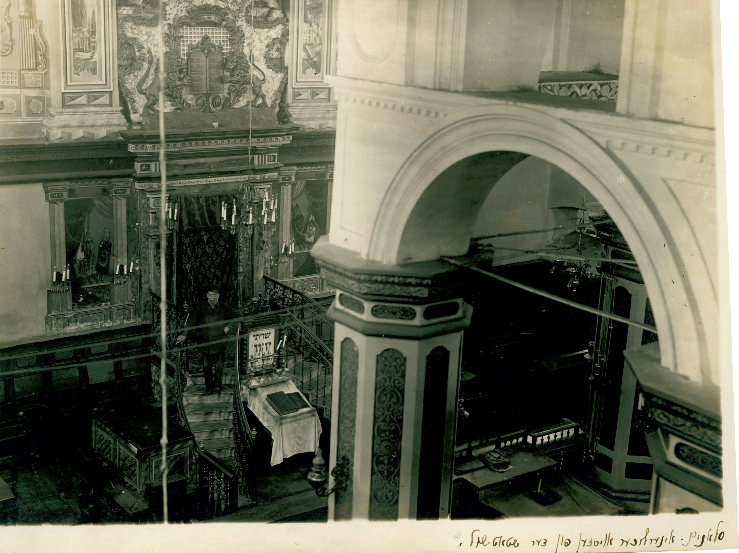 Black and white photo of interior of synagogue showing stone arch and column and rich decorations