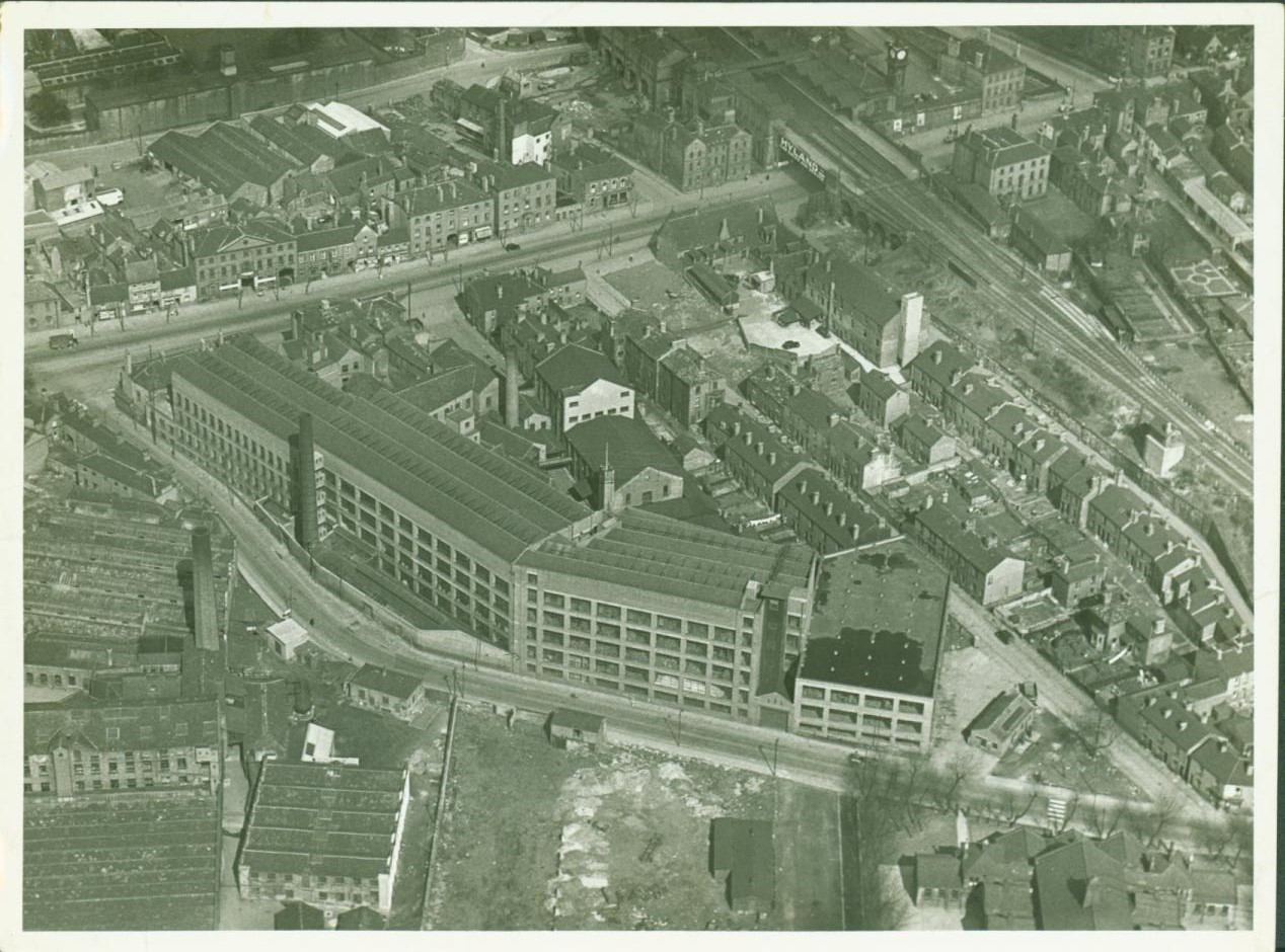 Black and white photograph showing the large building of the mill, and surrounding urban area.