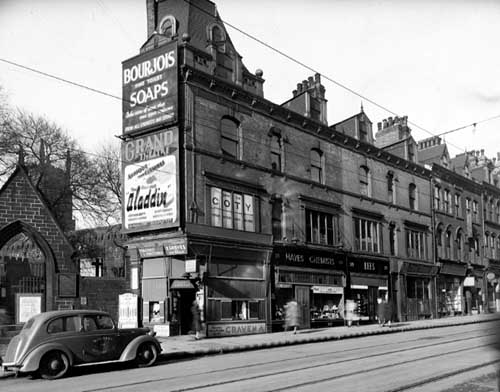 Black and white photograph of a street scene, with a car and shops.