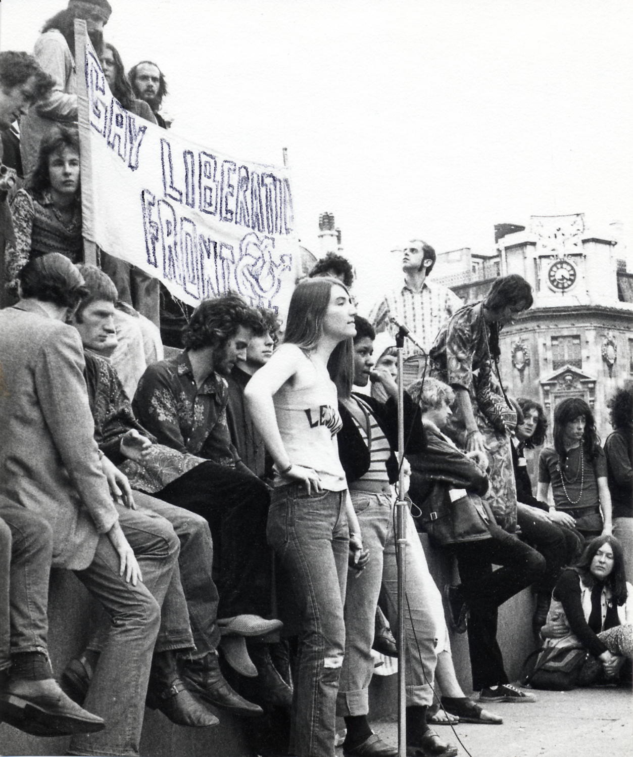 Black and white photograph of a crowd of people in Trafalgar Square, holding up a large home-made banner that reads 'Gay Liberation Front'