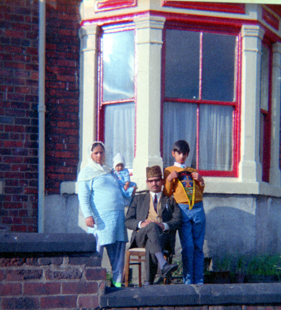 Colour photograph showing a man and woman with a young boy and a baby outside a house.
