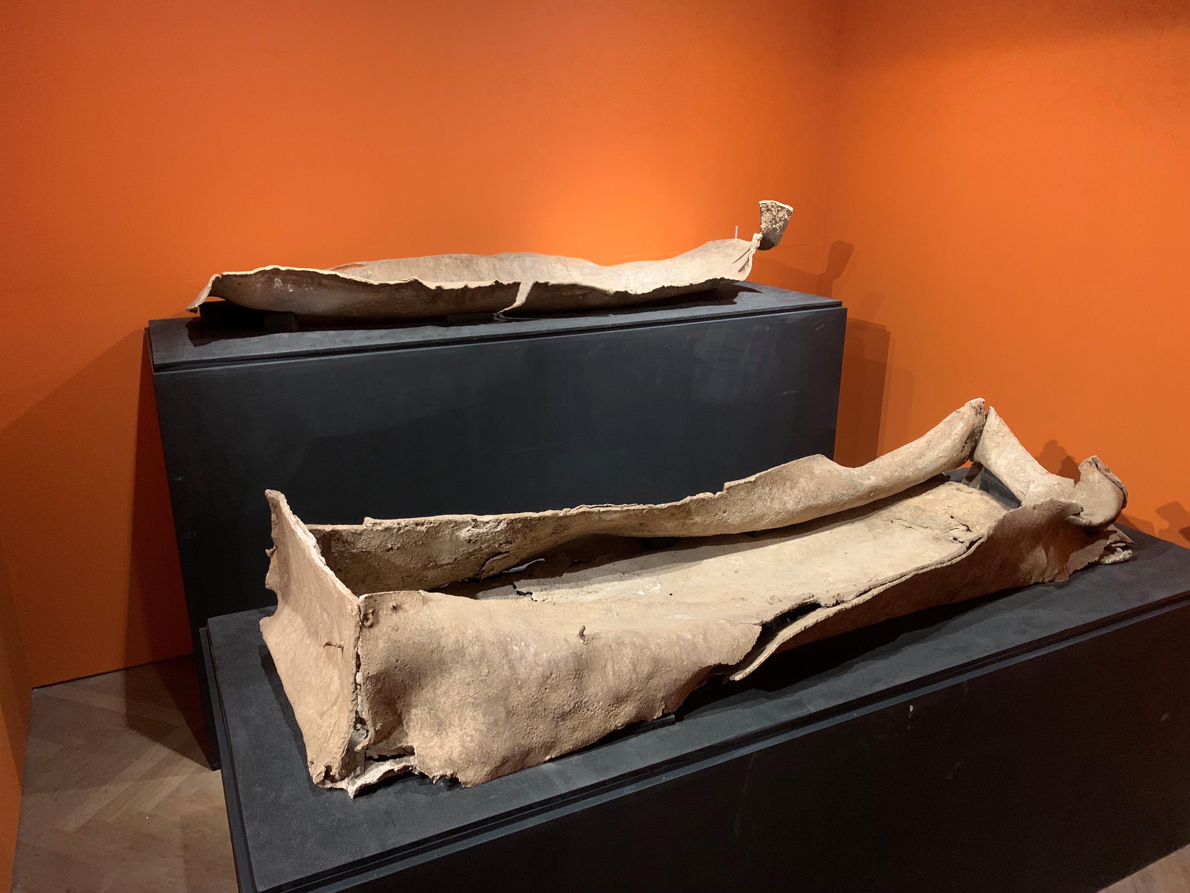 A Roman lead coffin. Previously a cuboid shape with base and lid, the sides have now collapsed due to age and appear more like a wet cardboard box, or leather.