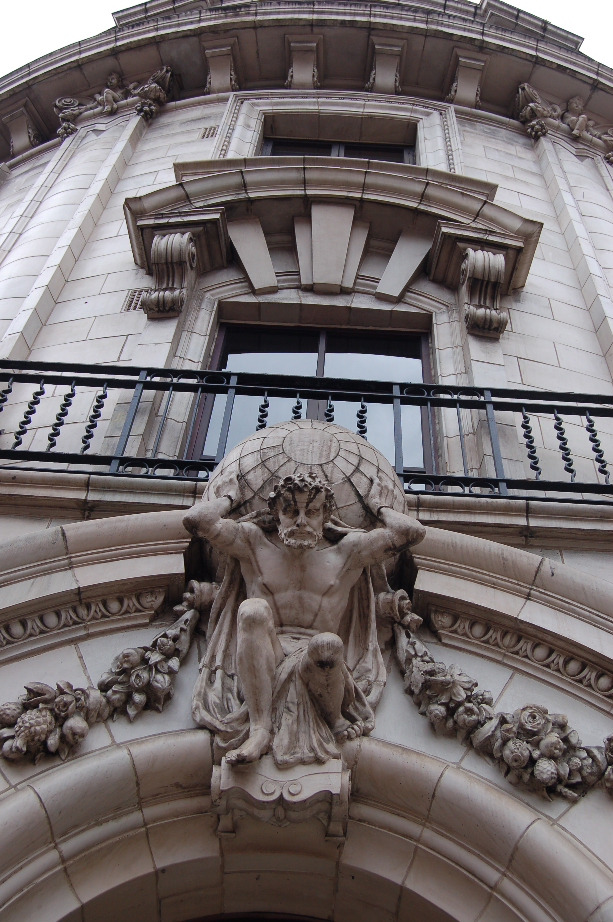 Contemporary photograph of a sculpture of Atlas, at the top of a building entranceway.  On his back is a stone globe shaped object.