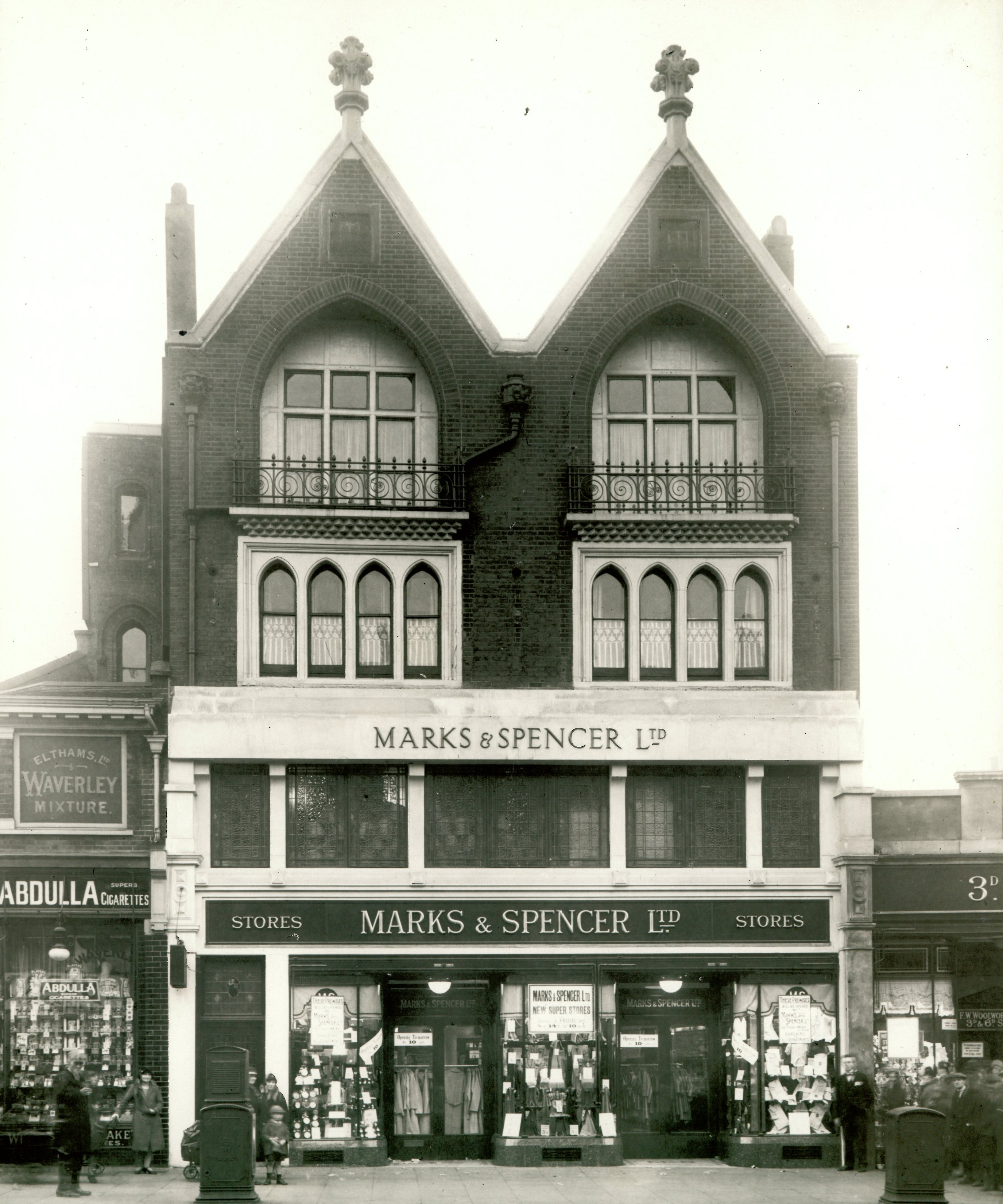 Black-and-white photo of a historic Marks & Spencer store with Gothic-style arched windows, signage, and product displays in the windows.
