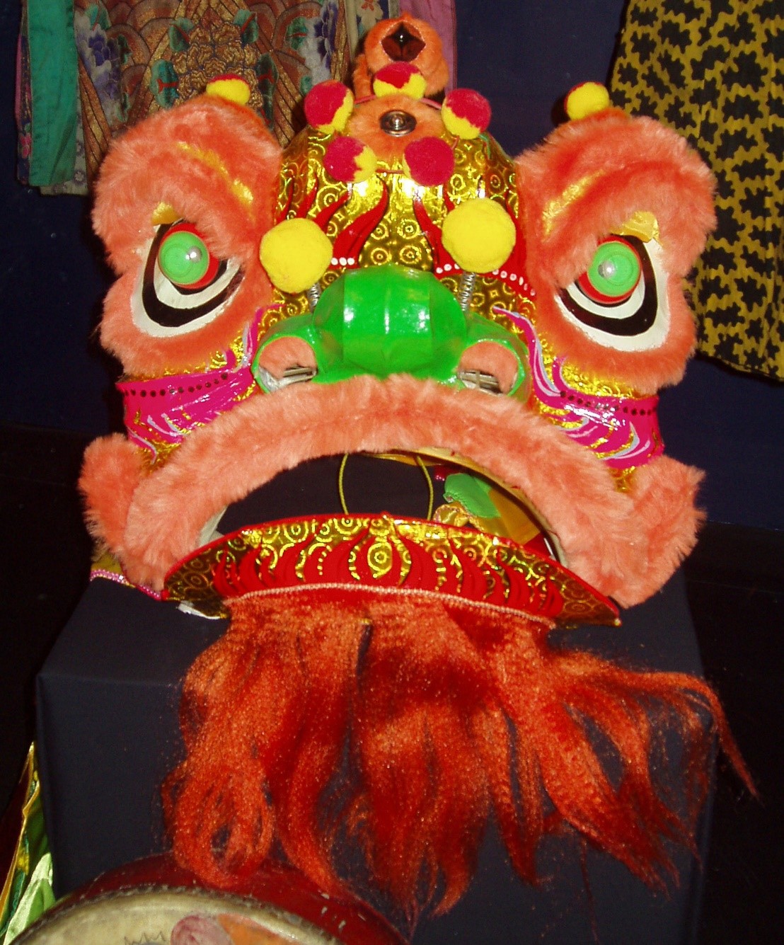 Large mask used for traditional Chinese lion dance. The lion is red pink and yellow with green eyes and nose and has a mouth that opens and closes.