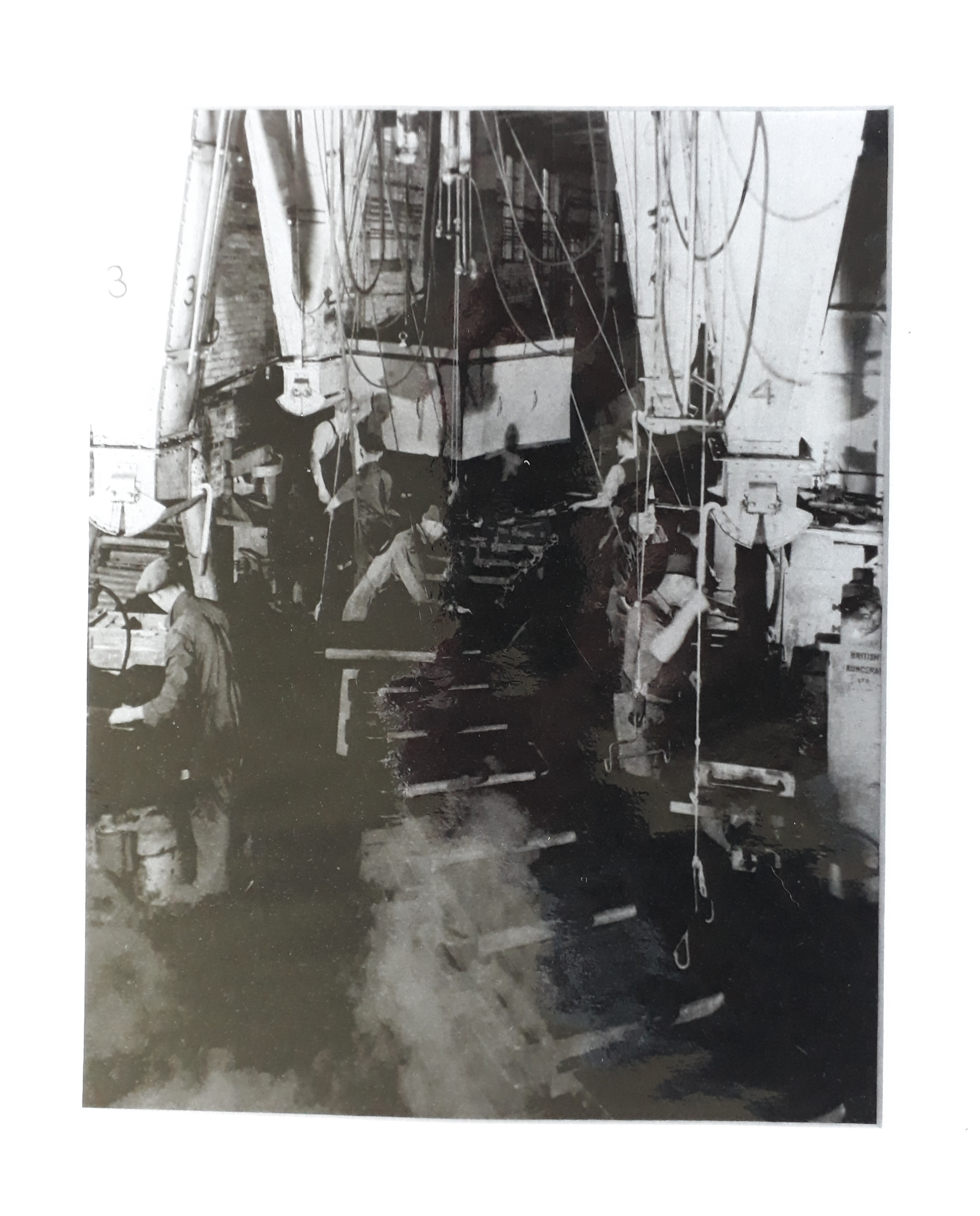 Black and white photograph showing men in a factory. They are wearing flatcaps and using machinery