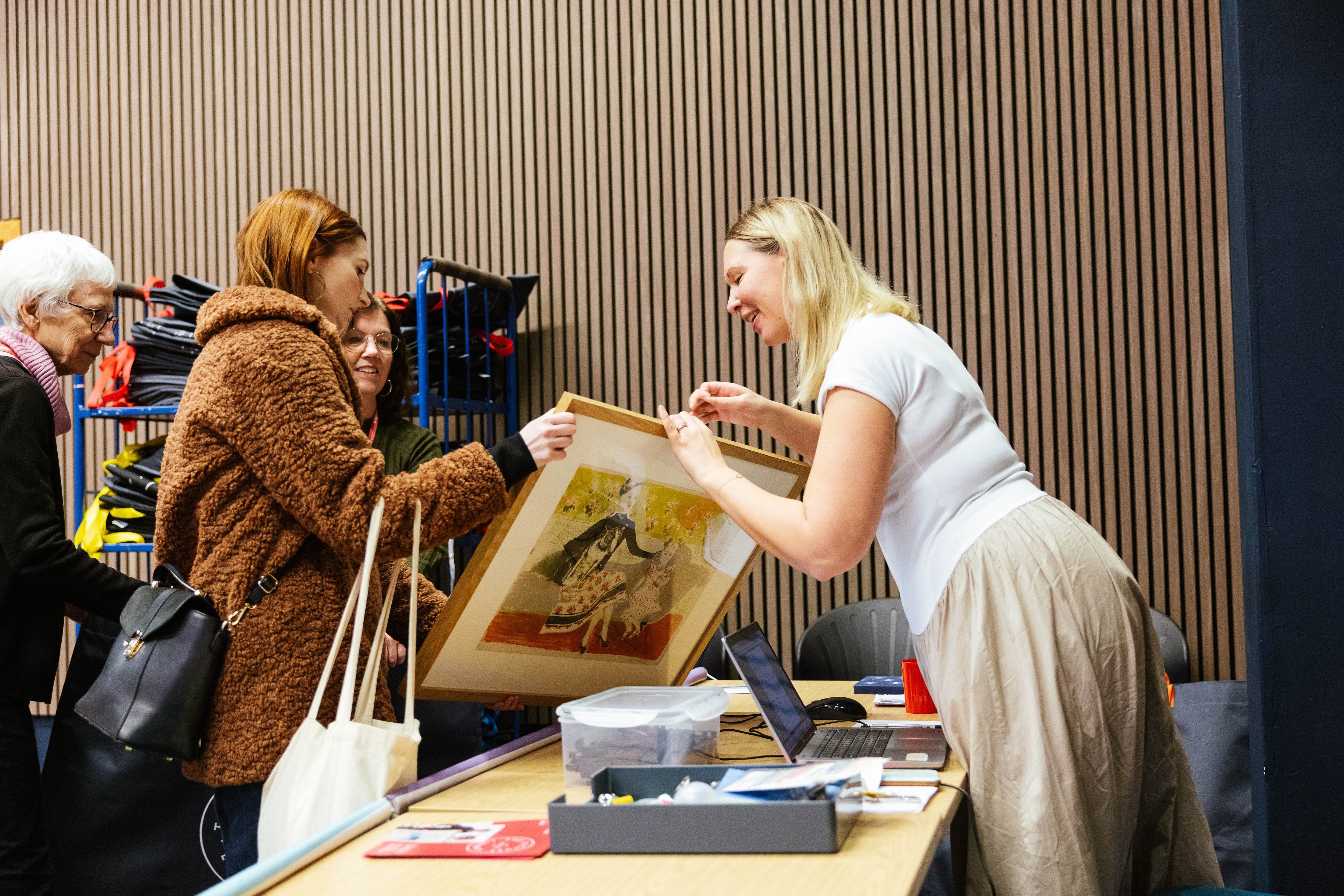 woman passing over picture to lady in big winter jacket