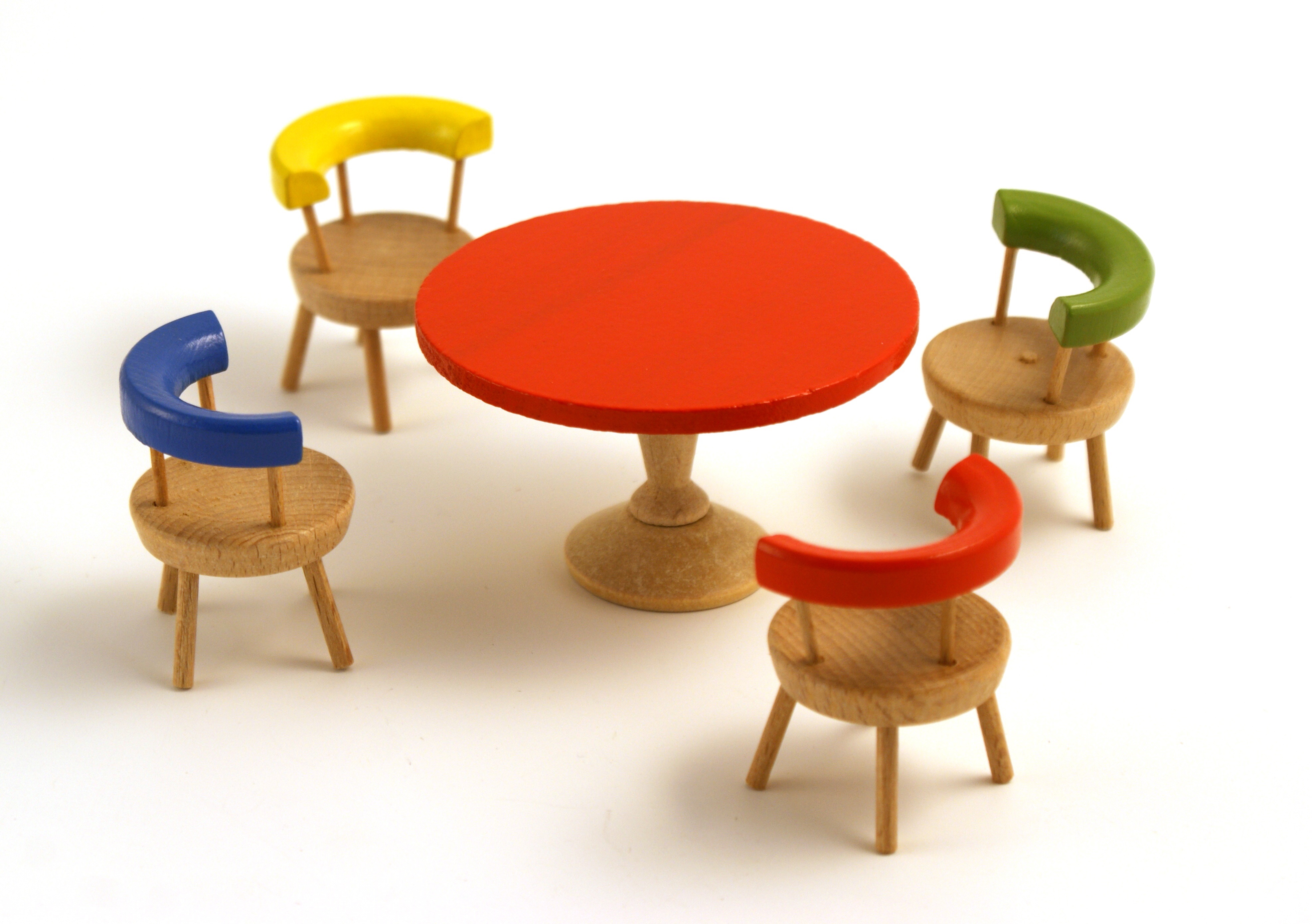 A wooden set of doll's house furniture, consistencing of a table with red circular top, surrounded by four chairs with circular seats and painted semi-circular backrests, in assorted colours, red, yellow, green and blue.