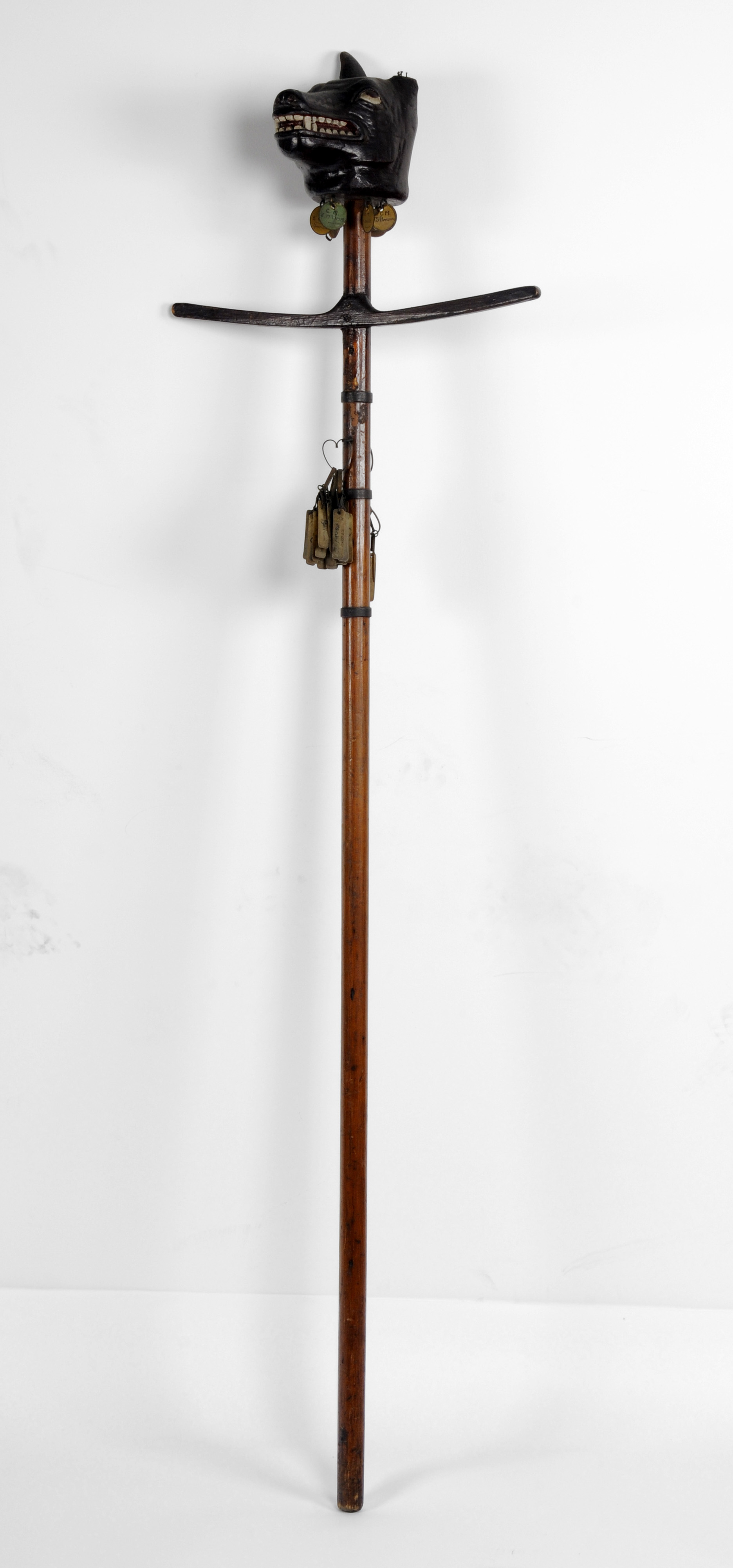 Wooden pole with carved head of a wolf on the top.  Metal tags hang from the pole, each one has a name on it.