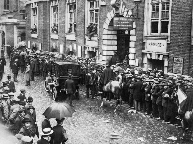 Black and white photograph showing queues of men outside a recruiting office in London.